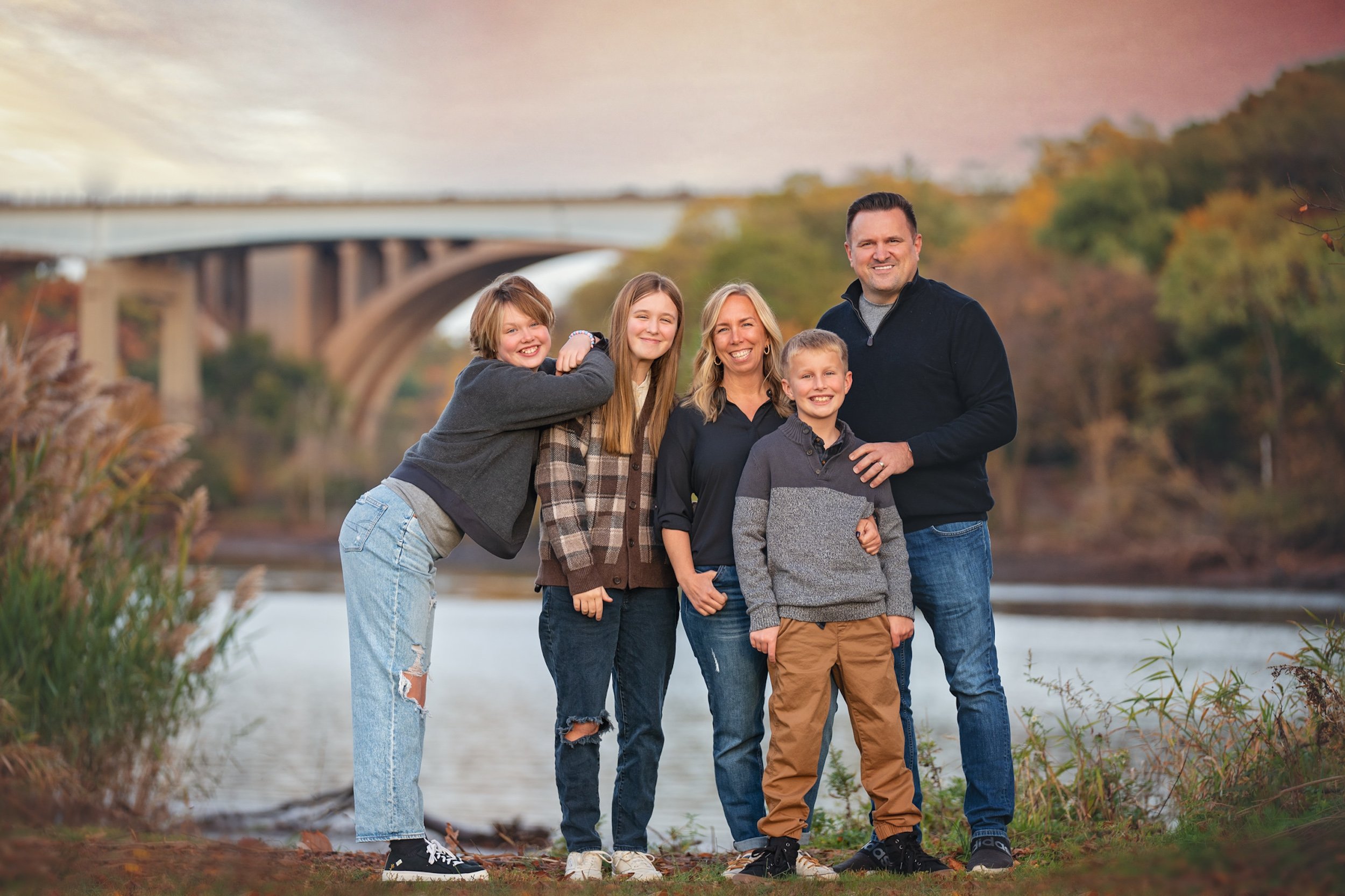 Family portrait during a fall outdoor photography session at Donaldson Park in Highland Park, New Jersey with autumn colors and the Raritan River in the background.