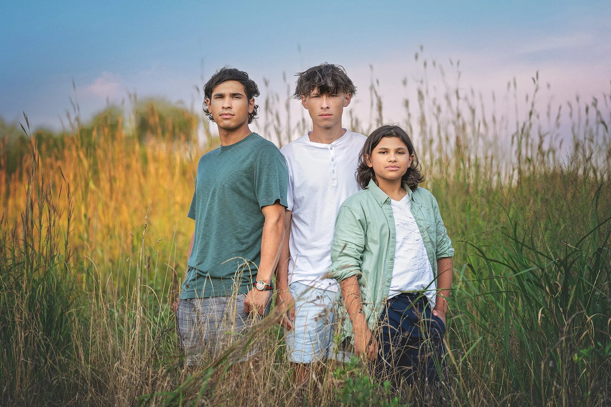 Outdoor family portrait of three brothers standing confidently in a tall grass field, photographed by Fotoplicity in Central New Jersey