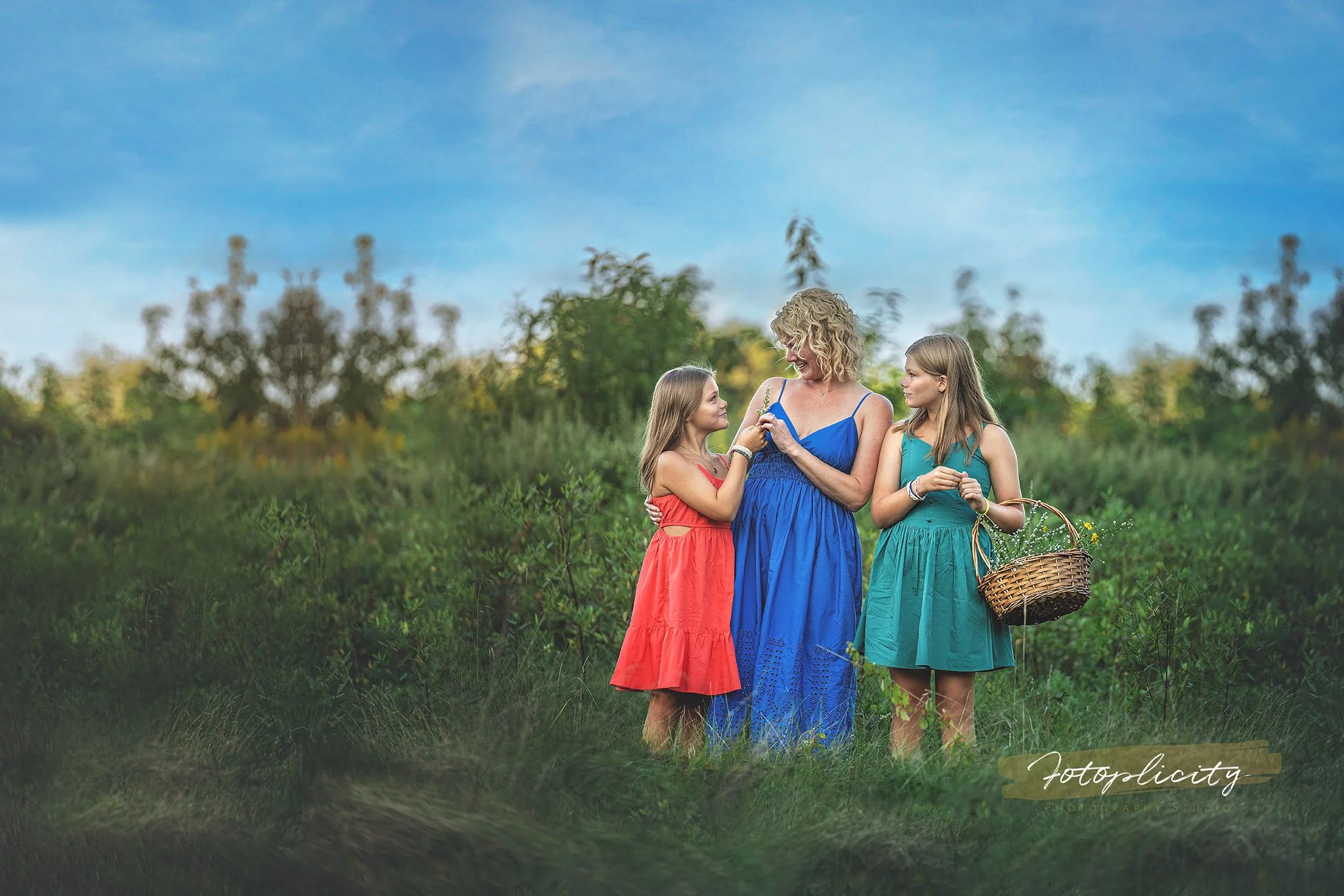 Mother and two daughters standing in a field, one daughter offering flowers and the other holding a basket, during a spring Mommy and Me session with Fotoplicity in New Jersey