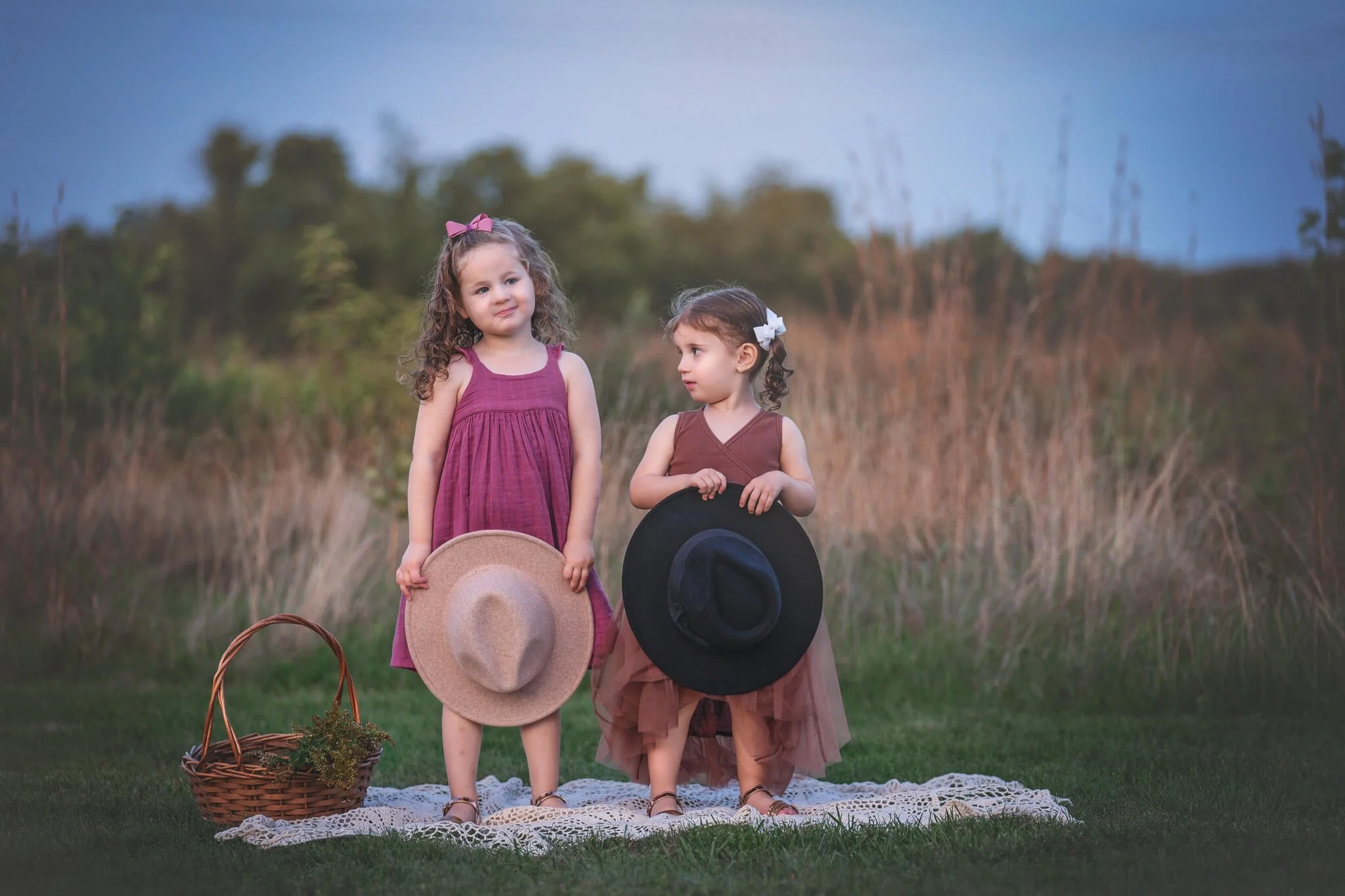 Two sisters standing together in a grassy field holding hats during an outdoor family photo session in North Brunswick, New Jersey.