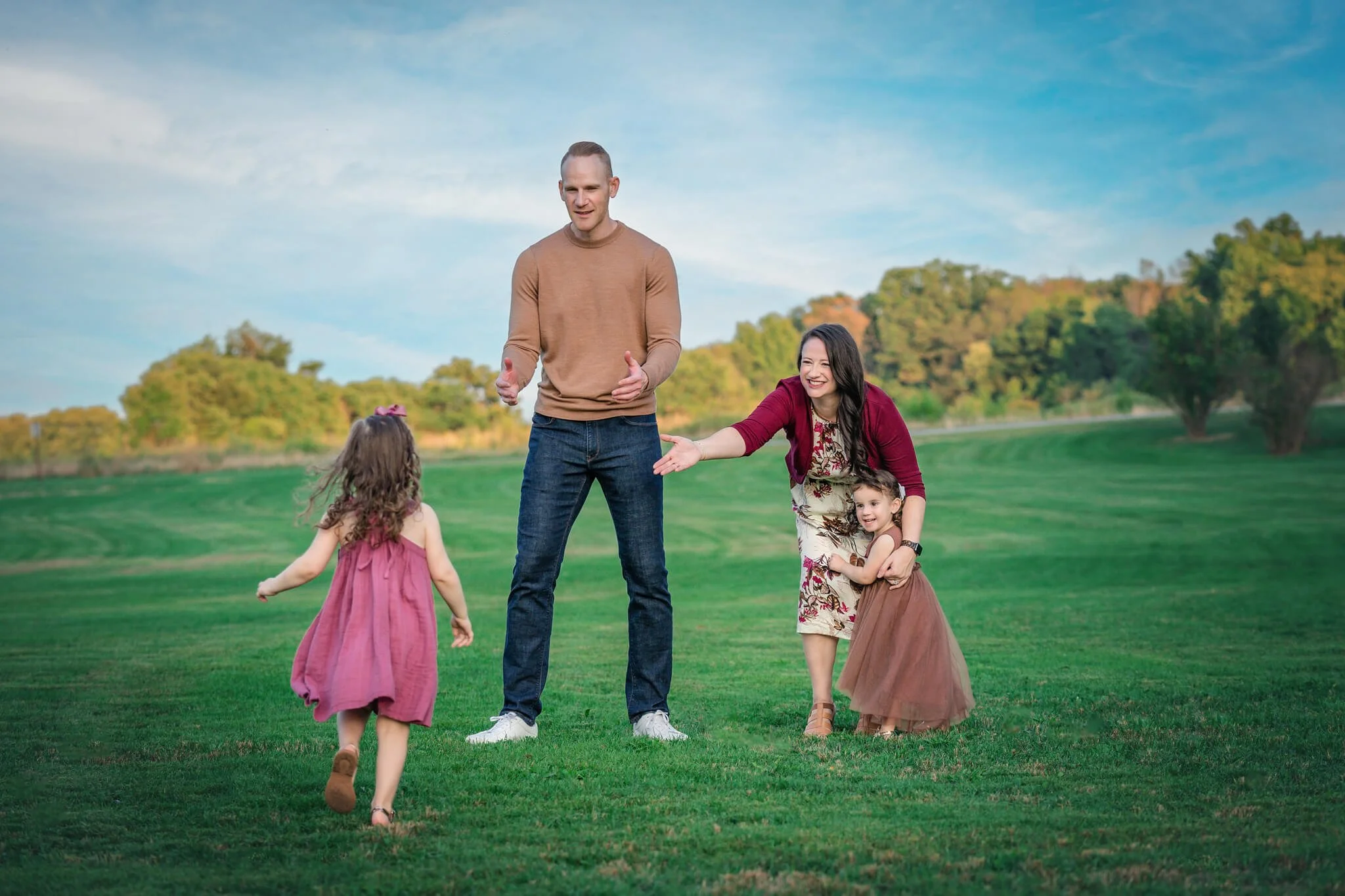 Parents playing with their daughters in an open field during a relaxed outdoor family photo session in North Brunswick, New Jersey.