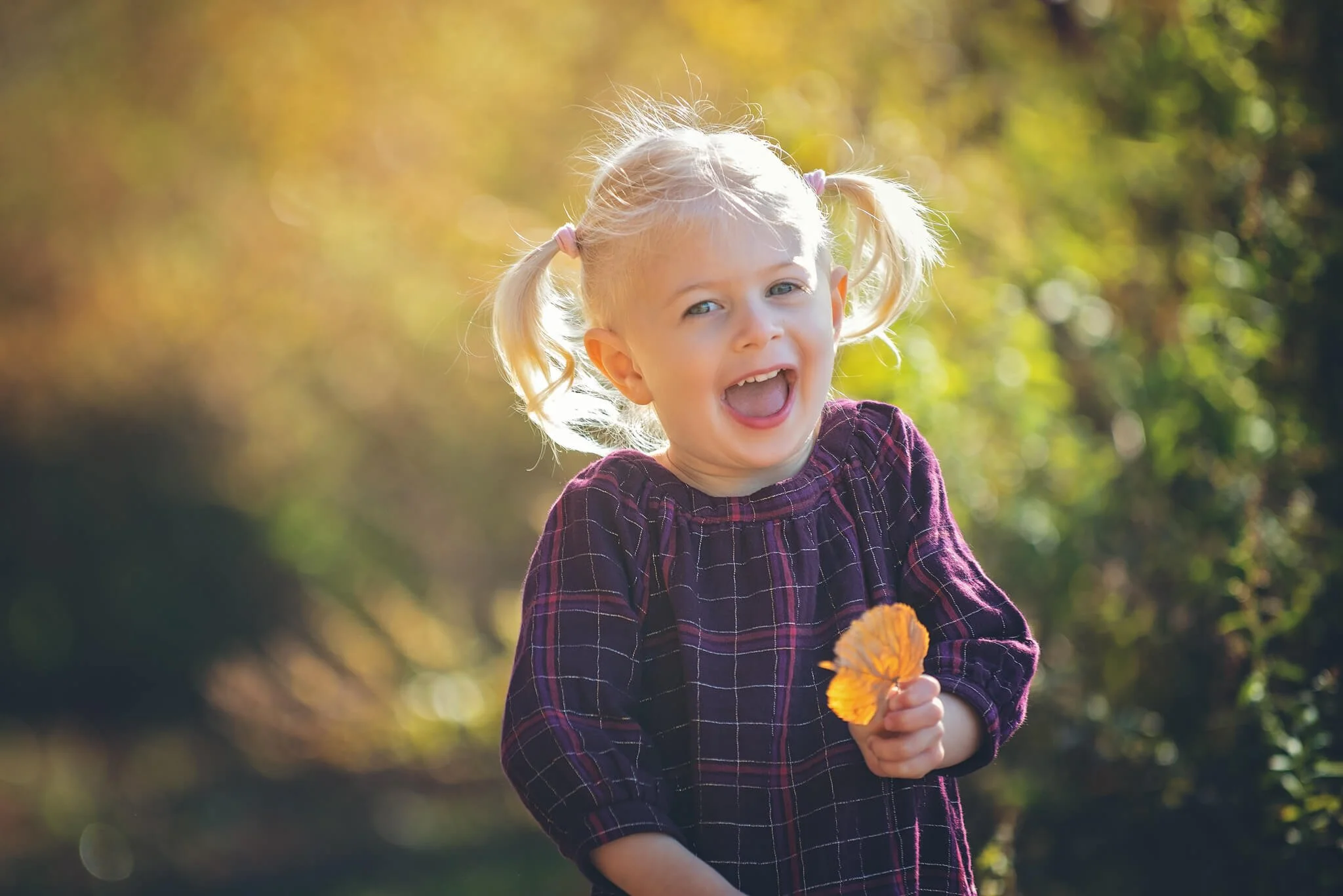 Smiling child holding a fall leaf during a golden hour birthday milestone photo session at Donaldson Park in Highland Park, New Jersey.