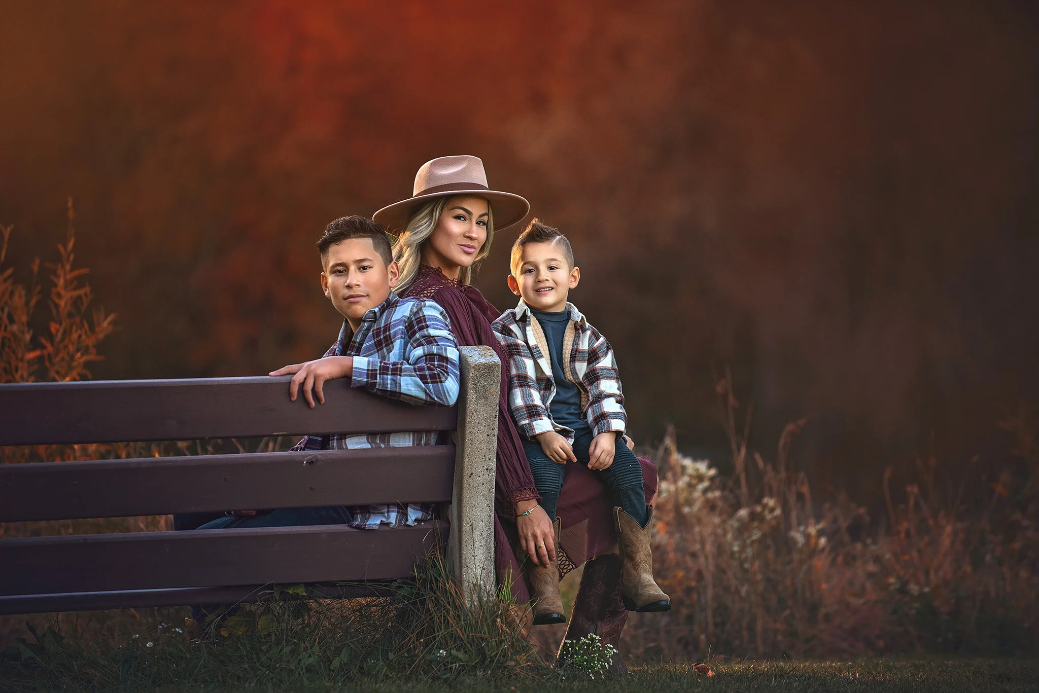 Outdoor family portrait of a mother and her two boys sitting on a bench at sunset surrounded by tall grasses, photographed by Fotoplicity in New Jersey