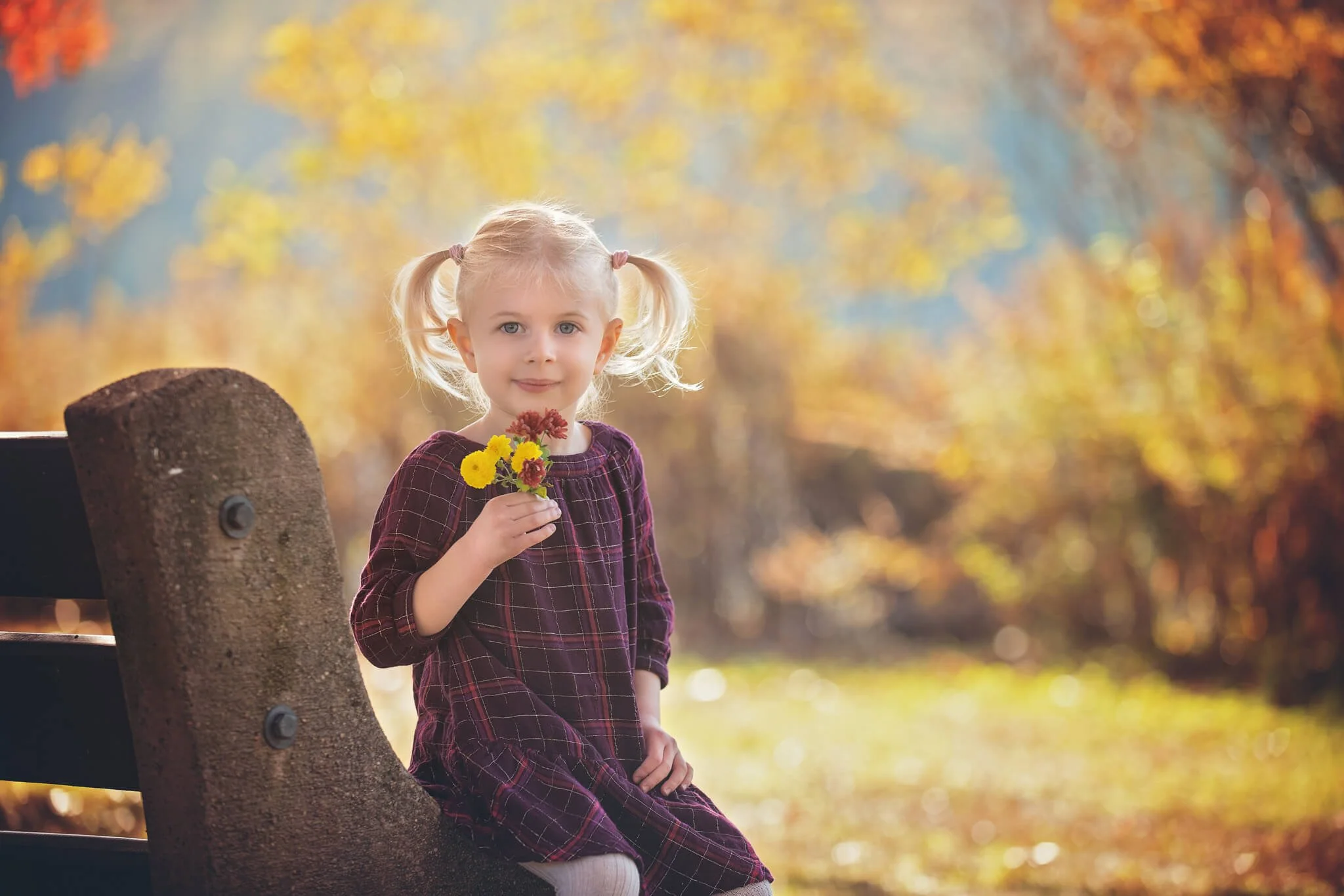 Young girl sitting on a park bench holding flowers during a Birthday Club portrait session at Donaldson Park in Highland Park, New Jersey