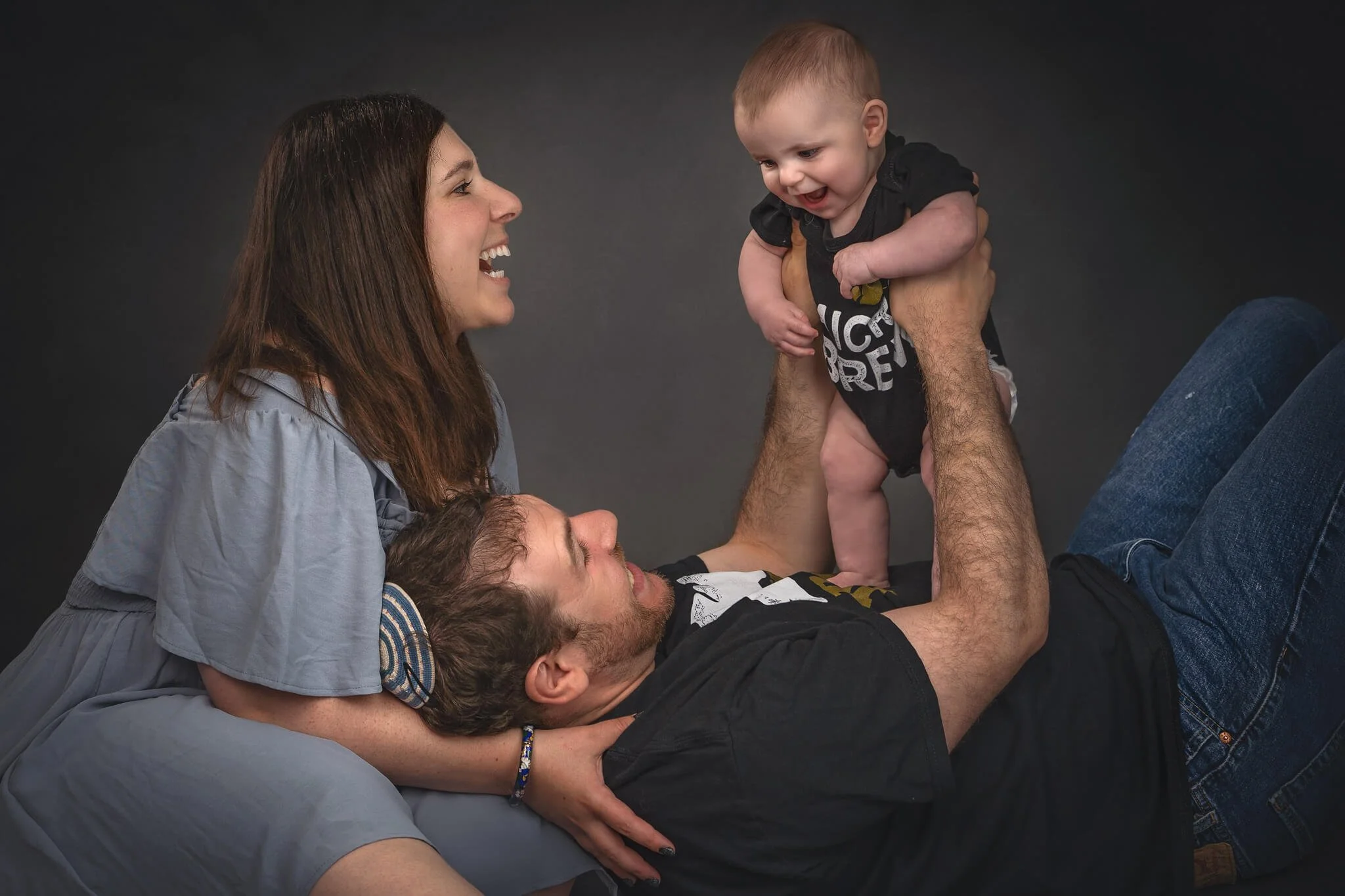 Candid family studio portrait — mom and dad laughing with baby at Fotoplicity studio, East Brunswick, NJ