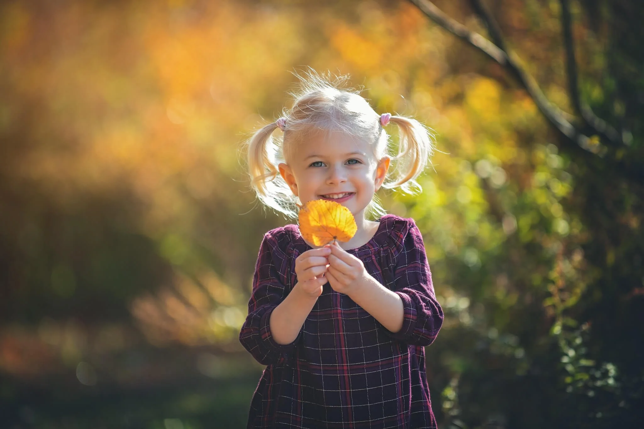 Happy child smiling and holding a fall leaf during a natural light birthday milestone photo session in Highland Park, New Jersey.