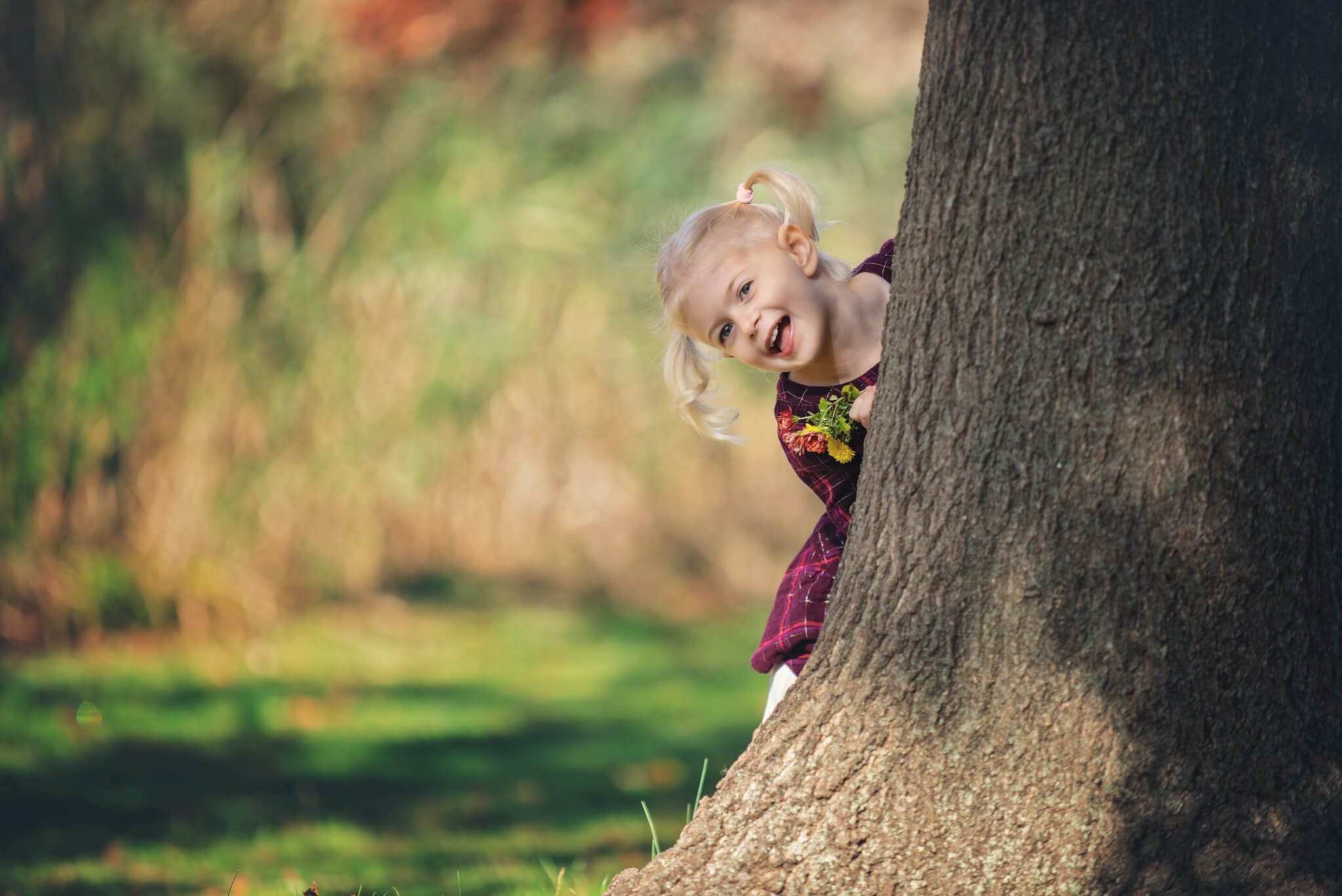 Playful child peeking from behind a tree during an outdoor birthday portrait session at Donaldson Park in Highland Park, New Jersey.