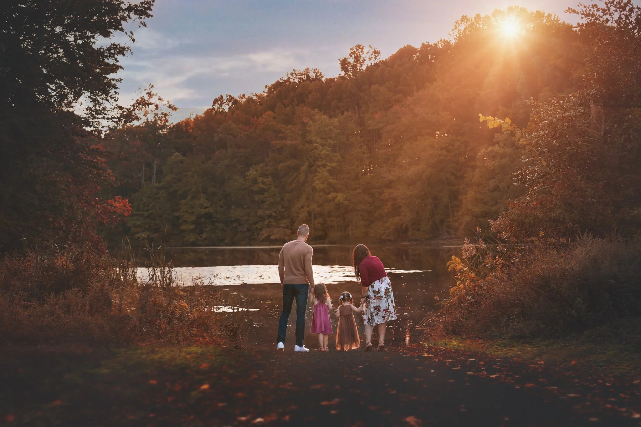 Family walking together along a lakeside path during a golden hour fall family photography session in North Brunswick, New Jersey.