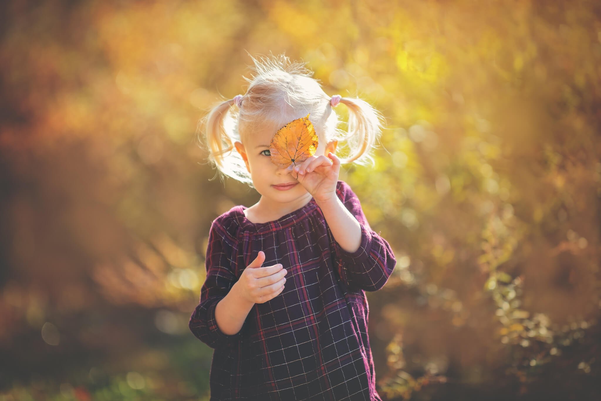 Young girl holding a fall leaf over her eye during a Birthday Club child portrait session at Donaldson Park in Highland Park, New Jersey.