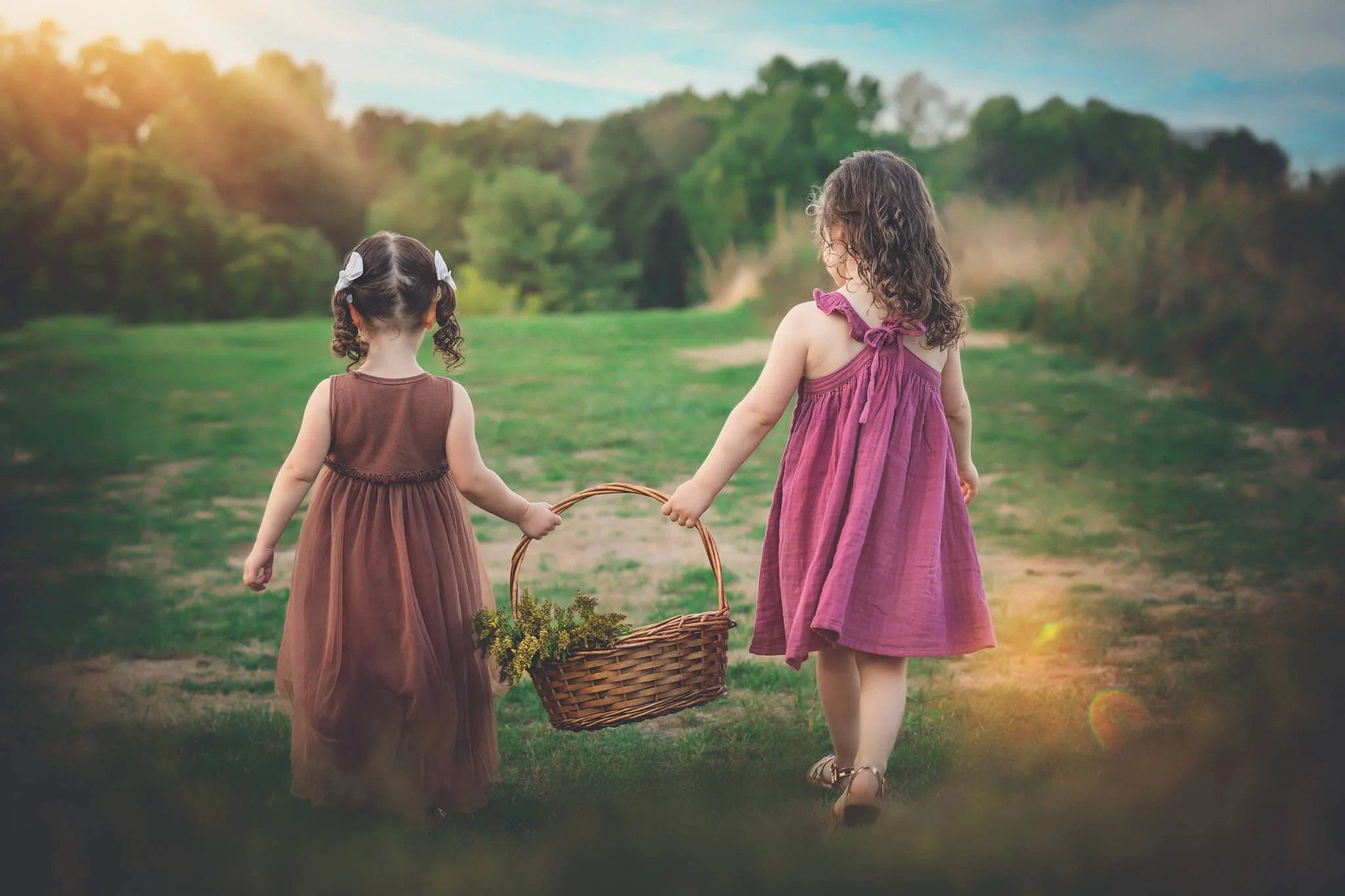 Two young sisters walking through a grassy field holding a basket during a golden hour family photography session in North Brunswick, New Jersey.
