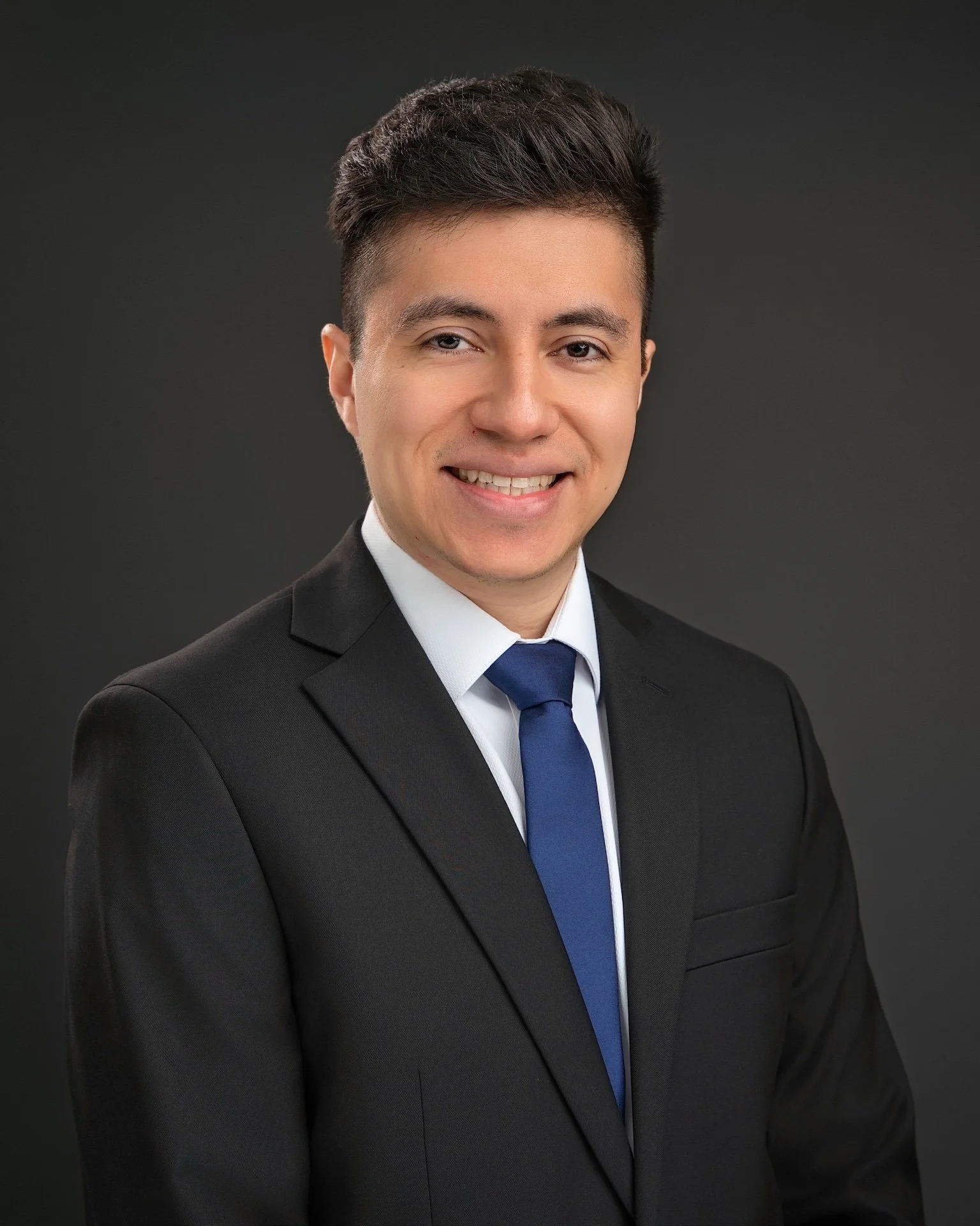 Professional headshot of a Rutgers student in a dark suit and blue tie, photographed against a dark gray background at Fotoplicity studio in East Brunswick, NJ