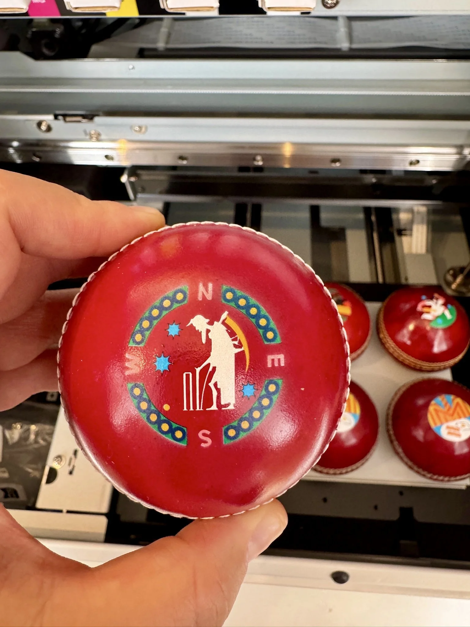 Close-up of a red cricket ball being printed with custom artwork