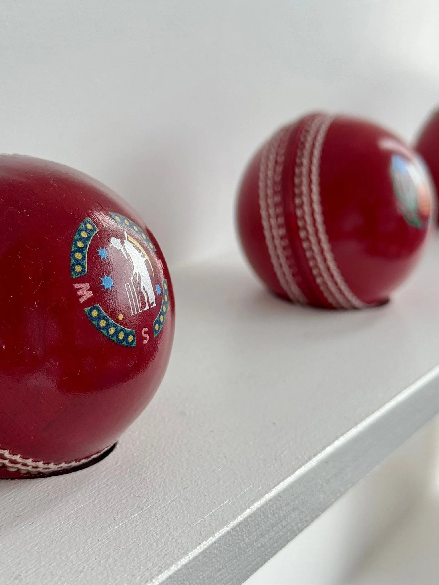 Red cricket balls featuring printed designs displayed on a white surface