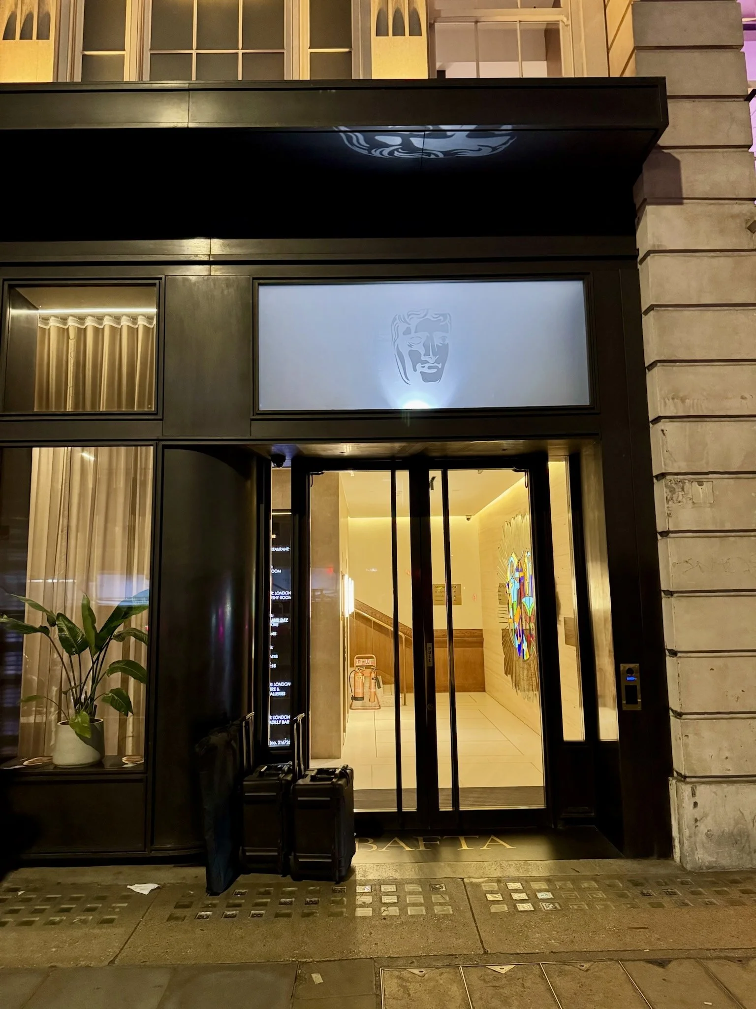 MakersCAFE BAFTA building entrance at night with illuminated glass doors and brand logo.