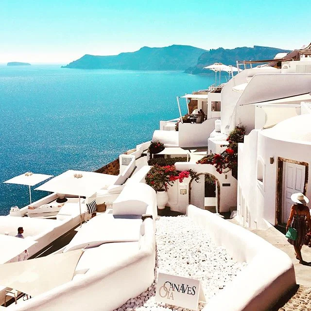 Santorini é extremamente turística. 
Há filas para tirar fotos, as turistas acordam maquiadas já as 7 da manhã e fica difícil aproveitar a paz de uma uma igrejinha mais rústica quando algumas garotas com vestidos esvoaçantes já estão penduradas no teto logo cedo, disputando espaço com seus paus de selfie... 😆 
Apesar disso, o charme do lugar é inegável. Com um pouco de obstinação (e paciência) é possível ouvir estórias dos locais e quebrar a camada superficial de futilidade para enxergar um pouquinho mais sobre a ilha.

Ainda estou trabalhando no post mas deixo aqui  umas poucas dicas para sair da mesmice (ou não) e tentar ver Santorini com outros olhos:

1. As casinhas brancas situadas nos penhascos, na verdade cavernas esculpidas na pedra (hoje mega valorizadas) eram antigamente depósitos de animais, adegas de vinho - ou presentes de casamento dado às filhas mulheres, sem muito valor de mercado. 
Hoje se transformaram em prestigiosos resorts de luxo - que não são baratos - mas valem cada centavo por proporcionar a tal sonhada paz que se espera usufruir em um local tão especial.

2. Tenha consciência de que 80% da experiência em Santorini dependerá de onde você se hospeda. Se você não tiver uma  vista para chamar de sua (de preferência com uma piscina infinita deslumbrante), você irá precisar disputar espaço nas ruas com uma multidão que irá se aglomerar para ver o por do sol, todos os dias.

3. Há uma trilha de Fira para Oia: são 10 km de estrada irregular e subidas, com vista para a caldeira (vulcão) oferecendo vistas maravilhosas. Achei um must fazer essa caminhada a pé. A diferença entre as 3 cidades principais (Fira, Imerovigli e Oia) não se vê tão facilmente, mas se sente perfeitamente uma vez por lá (são vibes completamente diferentes). 4. O sítio arqueológico de Akrotiri é um assentamento da Idade do Bronze destruído por volta de 1600 AC. que vale a pena ser visitado. É muito mais interessante se você contratar um guia.

5. Existe uma doceria (Melenio) com um terraço perfeito para fotografar as igrejinhas de cúpulas azuis. 
6. A menina da foto sou eu! Nos hospedamos em 3 resorts em locações bem diferentes e contamos tudo no blog em breve 😉