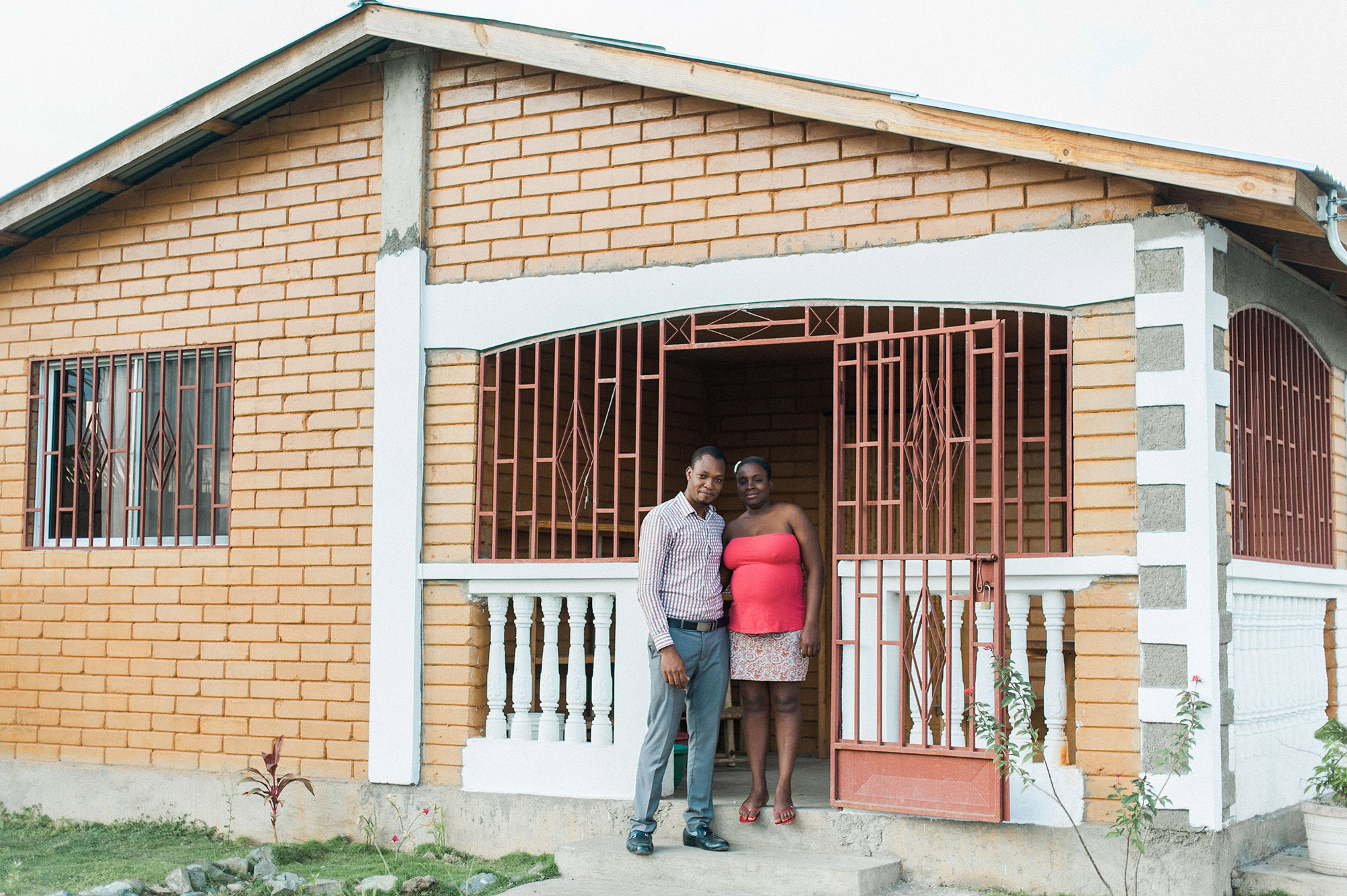 Manuacha and her husband stand on the front porch of their new earth block home, provided by PKF.