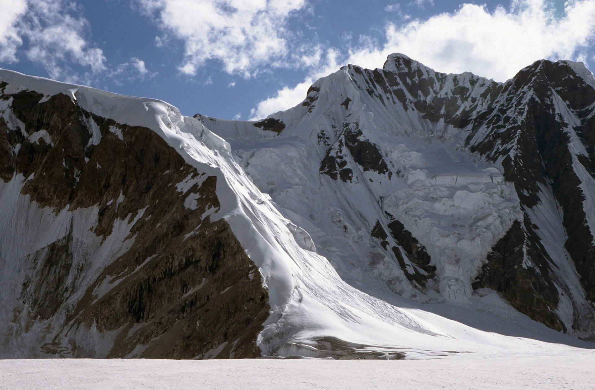 The Ghondogoro La 5,940m from the Ali Camp at 5,010m. The route follows the shadow in the centre of the photo. On Day 11, after sleepless and cold night at the Ali Camp, we started our ascent at 2 am. We crossed the glacier in roped teams looking out for hidden crevasses. We then started the 930m ascent arriving at the top of the pass at sunrise. We had beautiful weather and good visibility and low wind. We had to cross some funky sections with large seracs looming overhead. We also had to cross a few crevasses along the way up. Once on top, our porters smoked K2 cigarets and drank garlic tea that was supposed to be good for altitude. We took many photos and admired the early morning view. From the top, we could see K2 and the Gasherbrums rising from behind the nearby ridge. Four 8,000m mountains are visible from the pass. The view to the south was much better with Laila Peak rising majestically over the glacier below. This is one of the most spectacular passes in the Karakoram. The descent from the pass was steep and rocky. There was a fixed rope put in place and we could use it to repell down. The rockfall danger was present on this section of the descent. Once off the 50 degrees section of the descent, we could relax a little. We arrived at the Ghondogoro High Camp at 4,800m in mid afternoon. We were quite tired from two days of walking the the sleepless night.