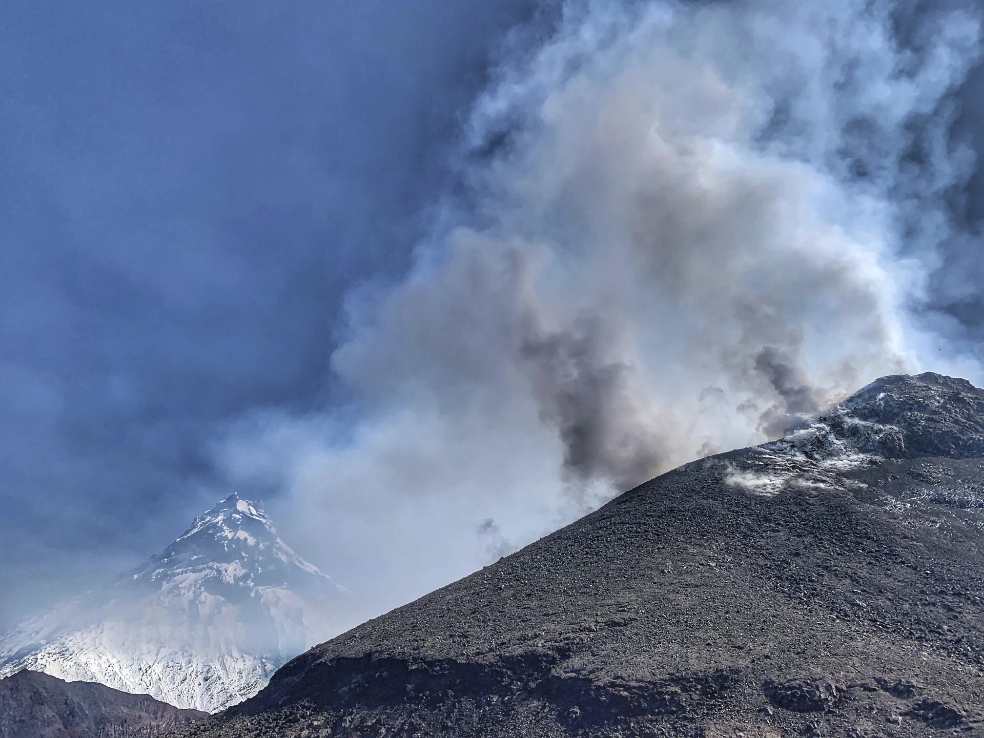 The smoking crater of the Bezimienny Volcano and the Kamienny Volcano towering above it. The Kamenny is obscured by volcanic ash.