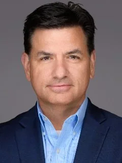 Professional portrait of a man in a navy suit coat, light blue shirt.