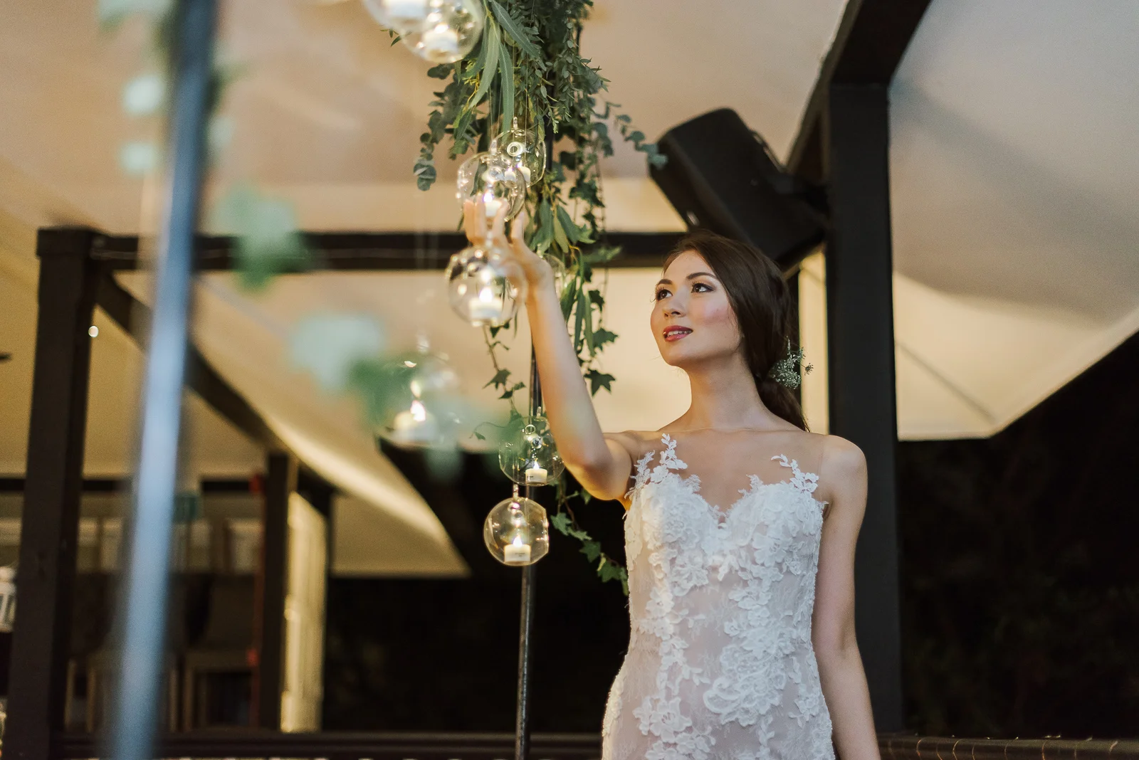 bride standing at rustic wedding backdrop of hanging glass orbs with candles