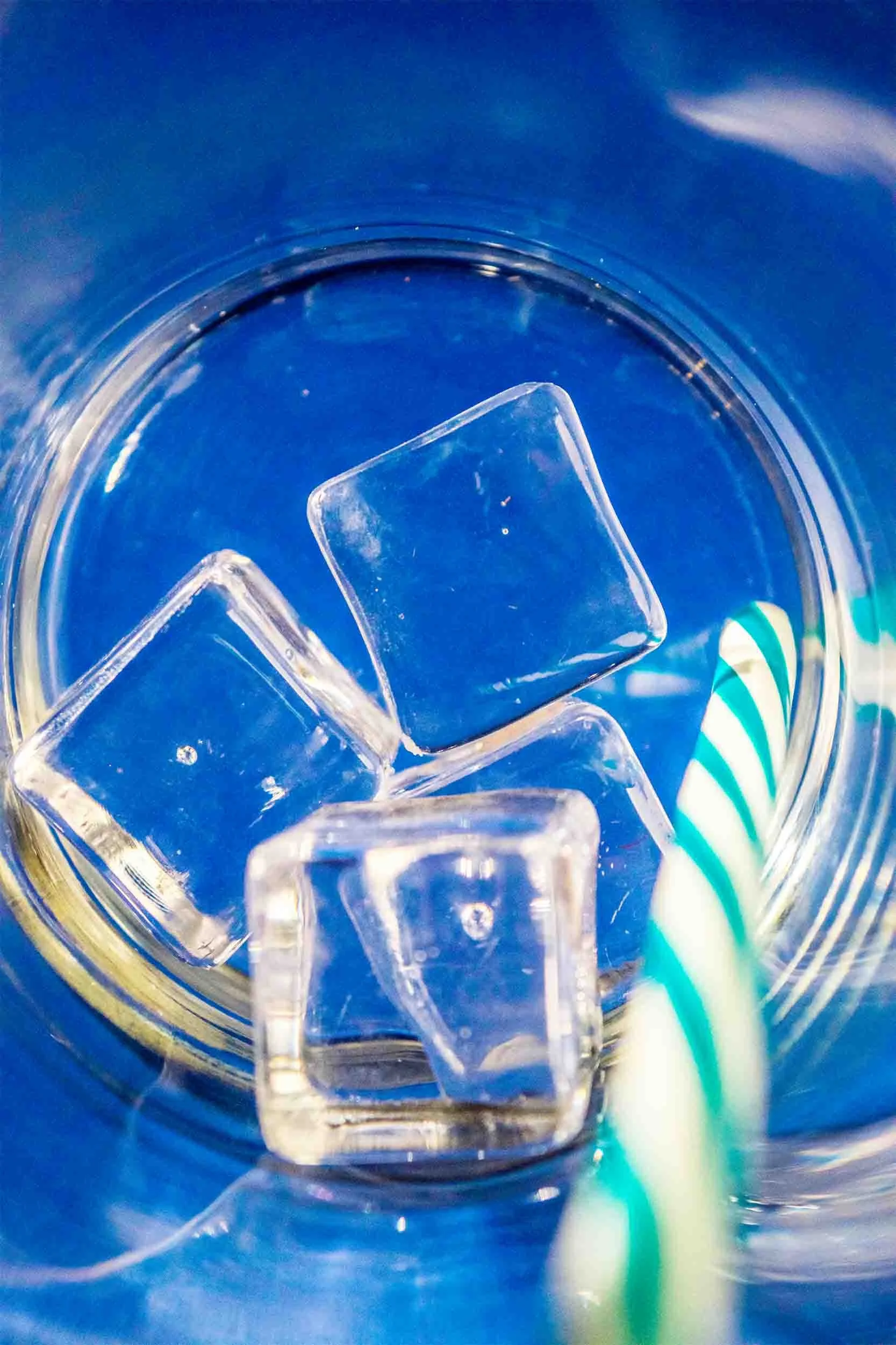 Ice cubes and a blue-and-white striped straw in a glass