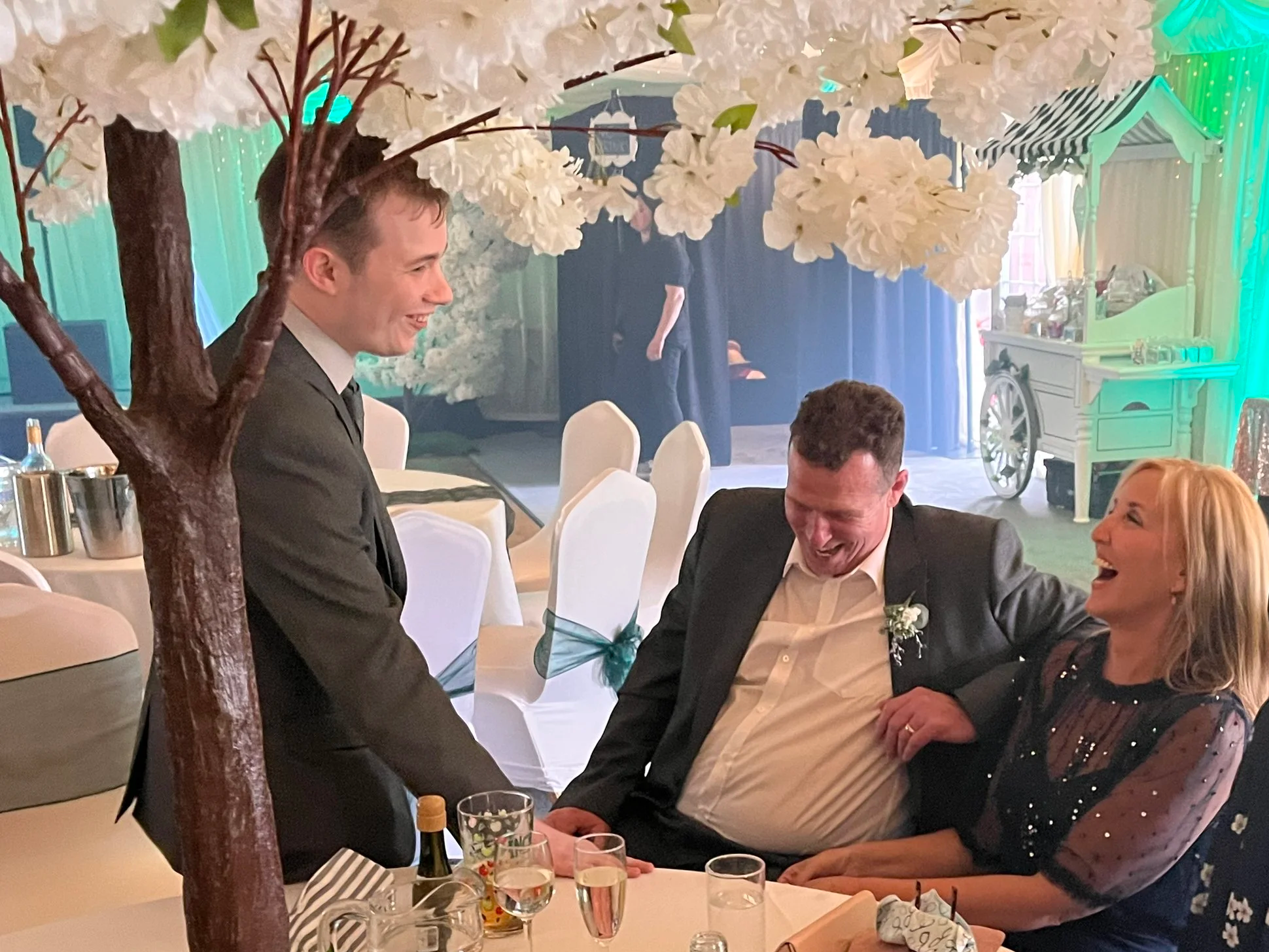 image of jaie standing next to two people at a wedding while that laugh and loo amazed.