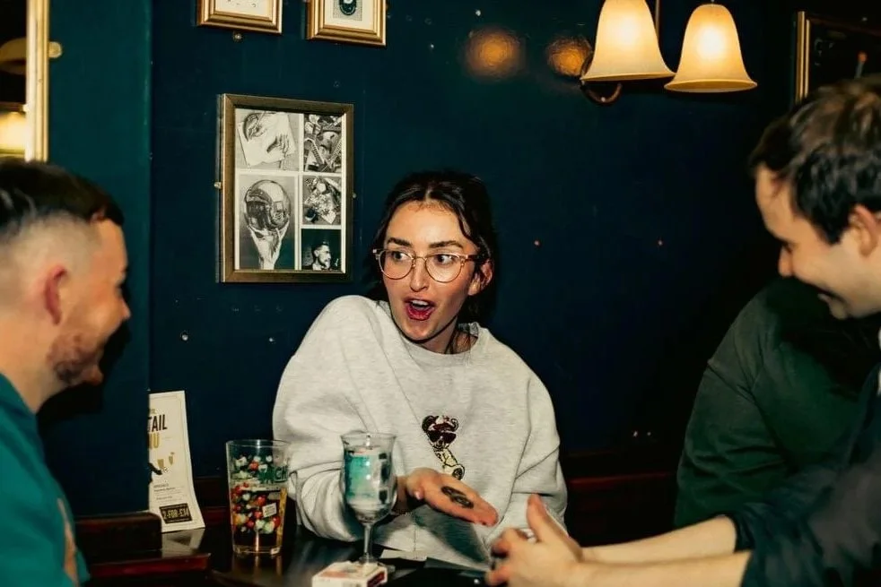 A woman with glasses excitedly shows a coin in her hand to two friends, amazed by a restaurant magician in Weston-super-mare