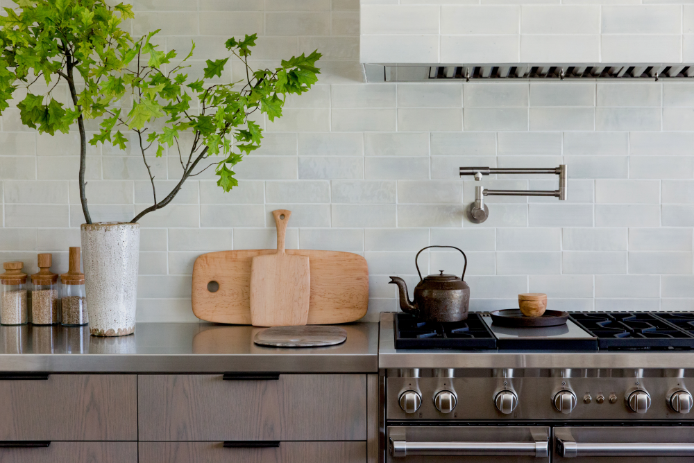 A closer look reveals a double stacked tile backsplash and matching range hood. By changing the traditional “brick stack” of the tile just slightly, so much visual interest is added! Speaking of unique details, this stainless steel countertop defies tradition and brings a touch of masculinity to the room.