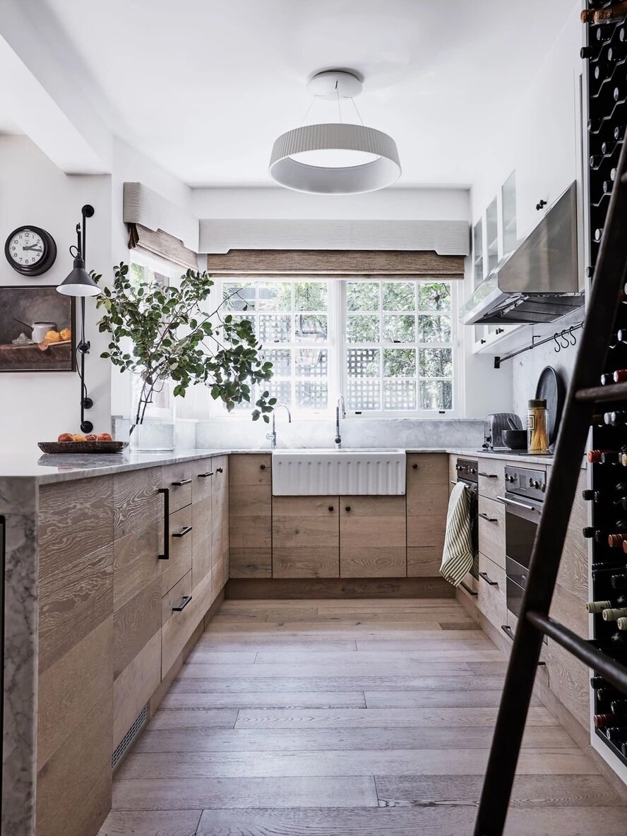 Fluted elements such as the oversized farmhouse sink and round lighting fixture overhead bring contrast to the mostly-wooded kitchen.