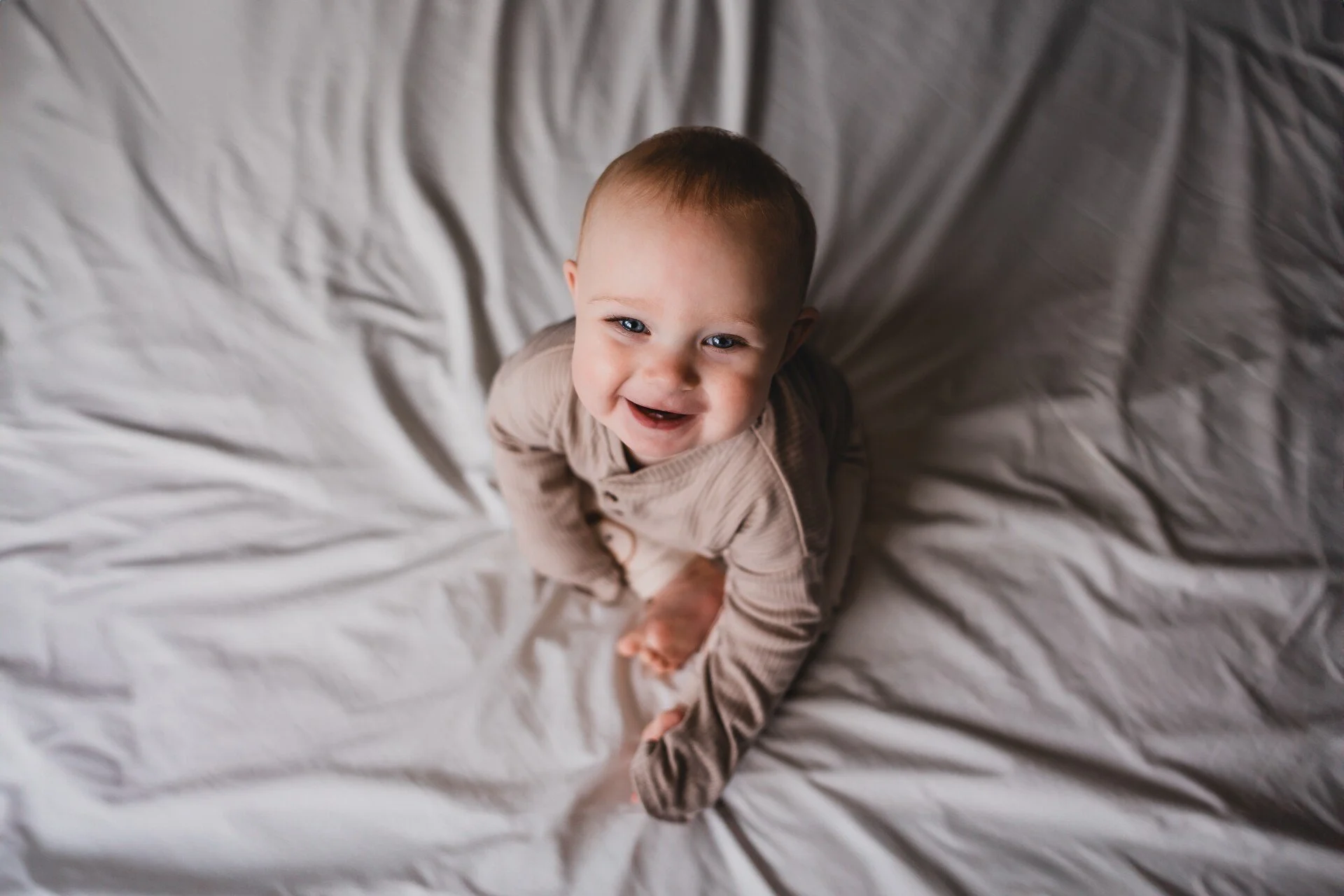 Baby sitting on bed smiling