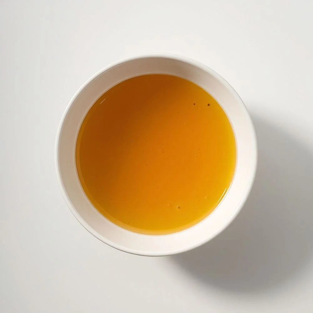 A plain white bowl of clear golden broth, shot from above