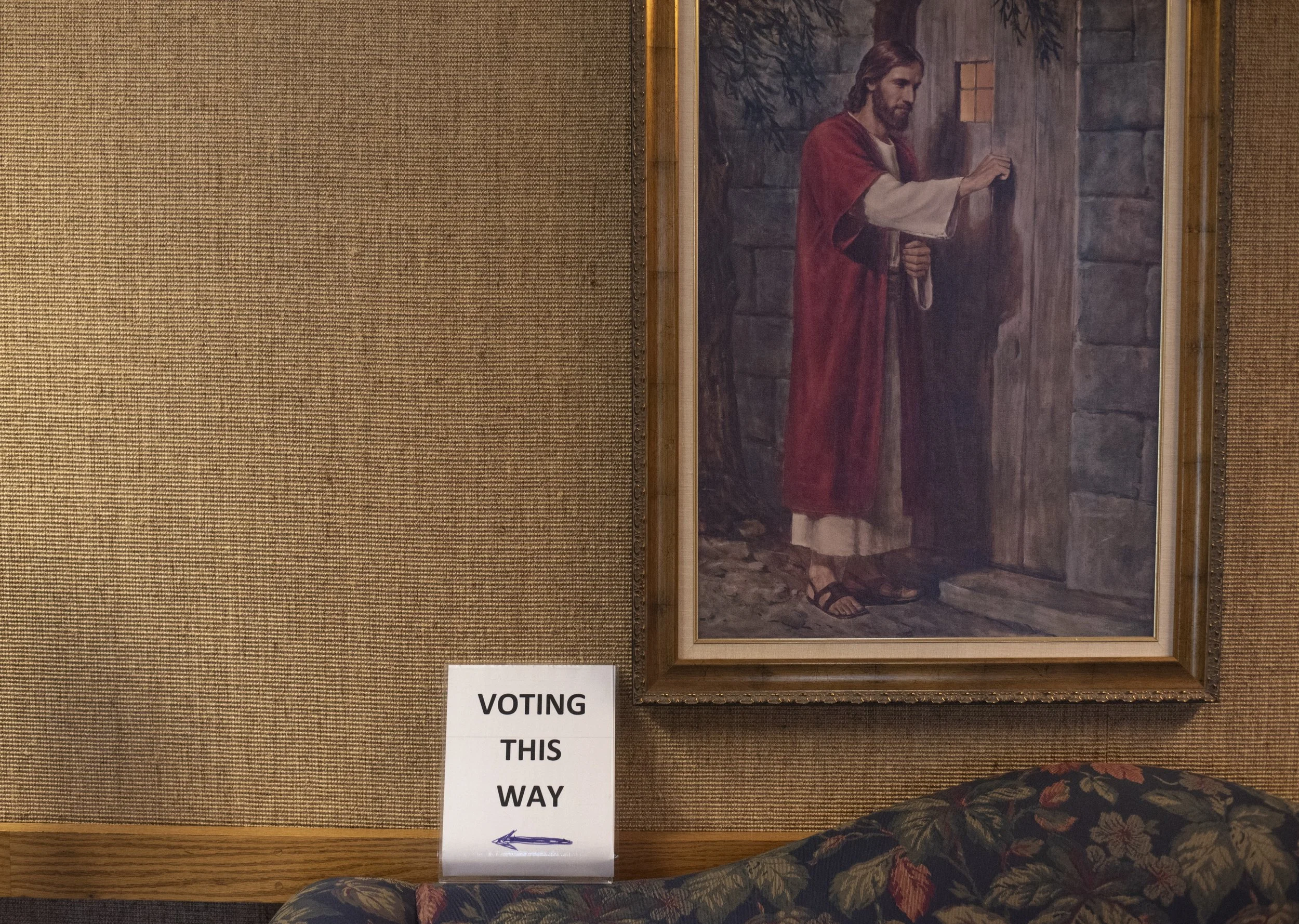  A sign that reads “Voting This Way” with a handwritten arrow sits next to a painting of Jesus Christ at Ward 1’s Church of Jesus Christ of Latter-Day Saints for the municipal elections in Laconia, N.H., Nov. 7, 2023. Polling locations are open 8am t