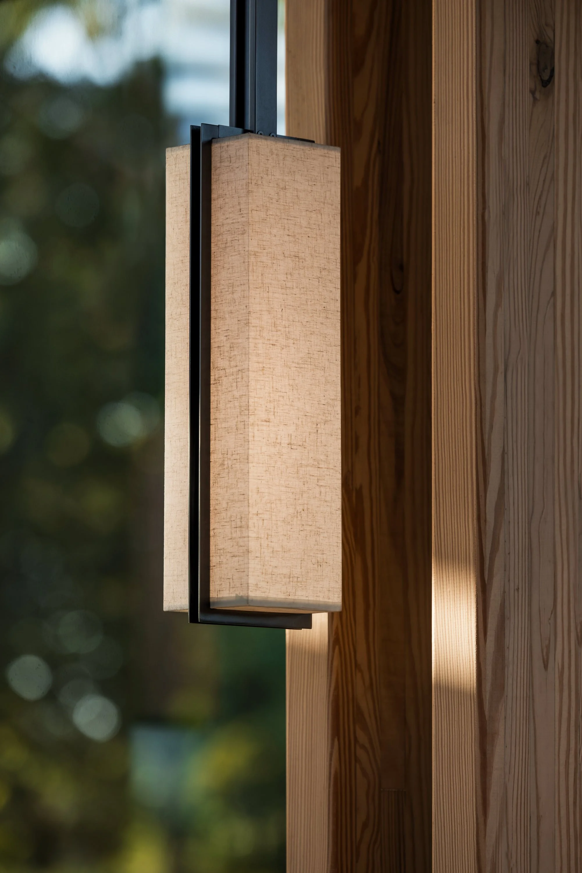 Close-up of a wall-mounted light fixture made of wood and metal, attached to a wooden wall with natural finish.