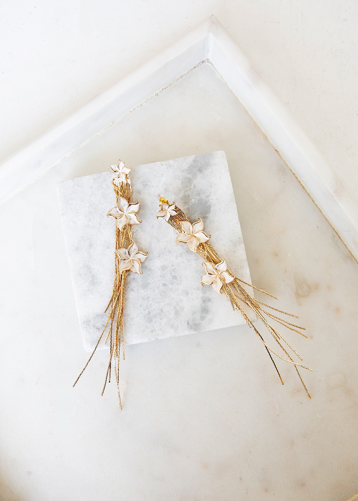 EDEN EARRINGS – The delicate Eden drop earrings are the perfect look for the contemporary bride on her wedding day. Cascading gold stands and three tiers of off white florals that frame the face.