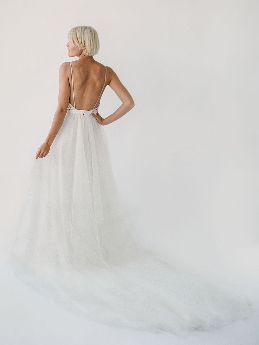 SARA. A beaded, v neck wedding dress with spaghetti straps. The cloud-like SARA dress is made with not one, not two, but three layers of our lightweight off-white tulle for a full and flowy skirt with an extra long train. In the front, cream beaded lace layers on taupe satin for an easy v neckline that feels oh-so soft against the skin. Meanwhile, in the back, cream beaded lace layers on a disappearing taupe mesh creating a cheeky illusion and tasteful open back. Hello dream dress!