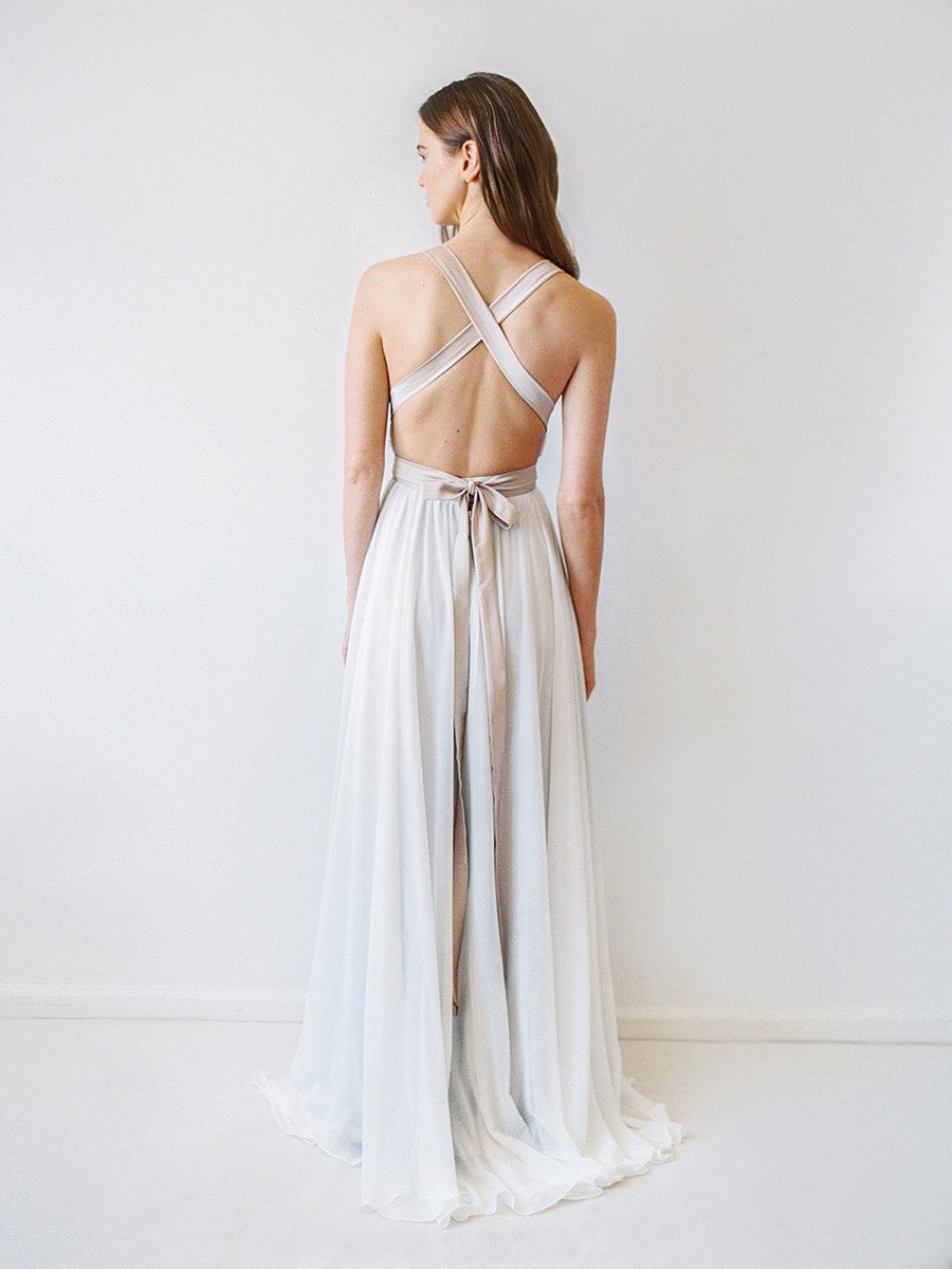 CARRALL. Whether on a Mediterranean island or lush meadow, exude confidence on your memorable day in the alluring CARRALL gown. Ribboned lace covers a plunging, v-necked bodice on this stunning, other-worldly gown. A twist on classic white, taupe lining rests underneath this off-white gown creating a dreamy colour-contrast. She is further highlighted with a satin ribbon that crosses and ties in a bow elegantly, perfectly showcasing a bride's back and shoulders.
