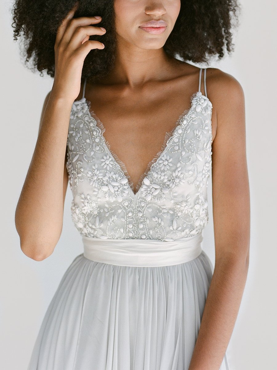 ALEXANDRA features a plunging neckline, open sides, and a striking back. The layered pick-up skirt is constructed with hand-draped chiffon, which catches movement and the wind perfectly. The bodice showcases hand-sewn Spanish lace and refined double straps. With its refreshing colour palette and unique fabrication, Alexandra is perfect for a cloudy day at the beach or a winter wedding. This gown is tied together beautifully with a silk bow that is both elegant and dramatic.