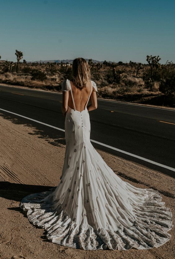 STEVIE is an embroidered chiffon wedding gown that is possibly as romantic as it gets. The gown features a 90s scoop like neck with flattering seams throughout the empire waist that flatter the hips and cascades into a dramatic rounded train. This dress also includes a fully exposed back with braided straps, flutter cap sleeve and two detachable flowing chiffon panels at the lower back. This dress can be half-lined for a sheer underneath look, see different styled photos for look.
