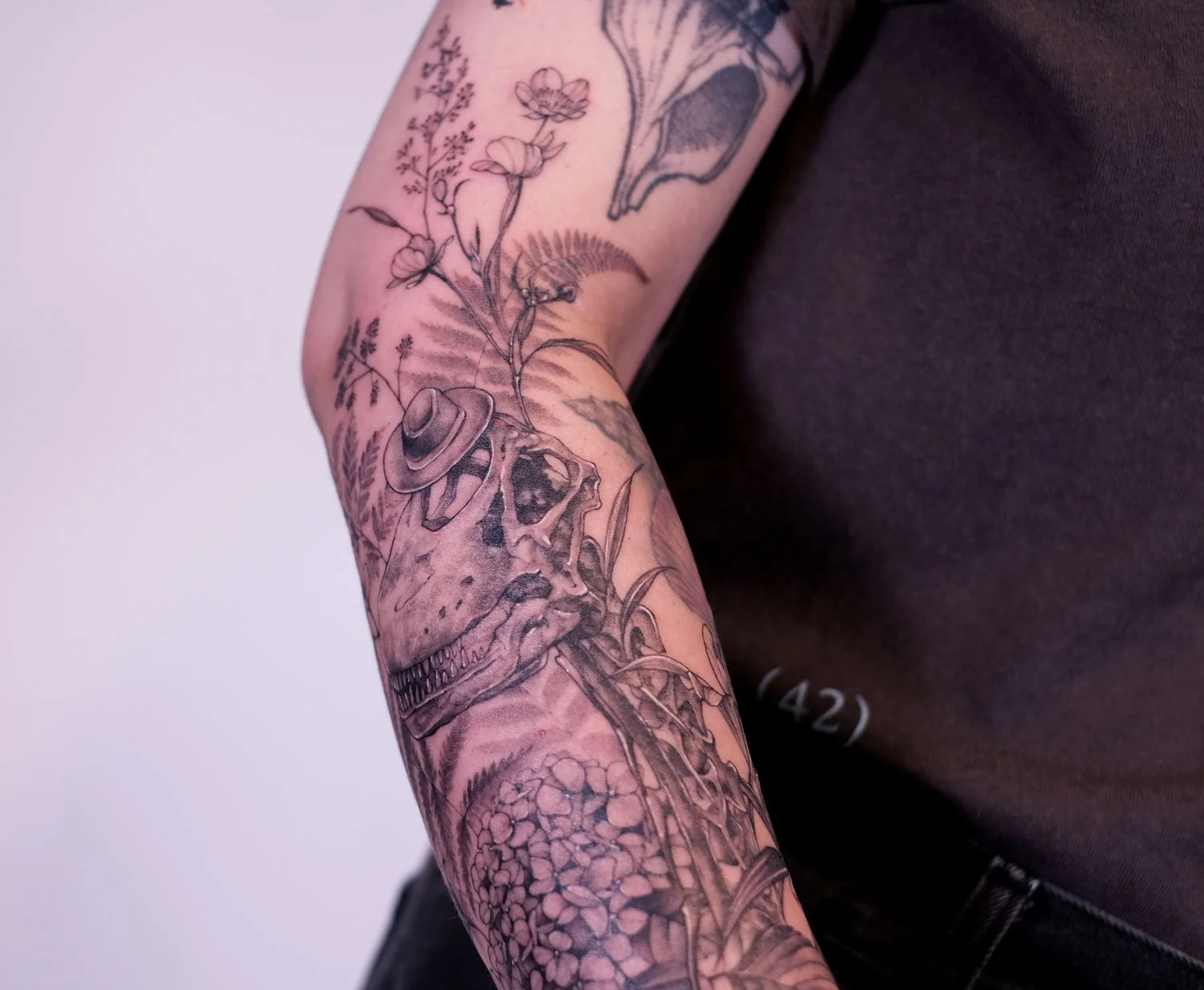 Fineline arm sleeve tattoo of The Last of Us II video game with Joel's funeral flowers and T-rex skeleton.