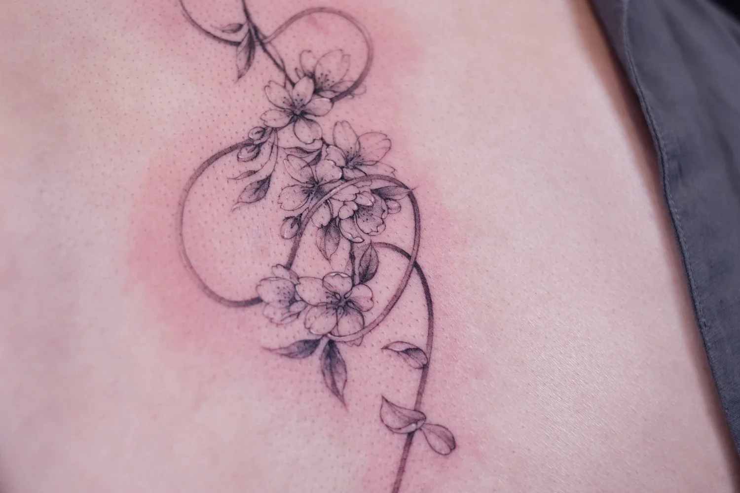 Fineline tattoo of sakura flowers and a rope.