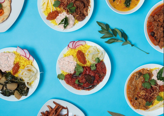 Assorted Indian dishes, including curries and rice, served on small white plates on a blue background.