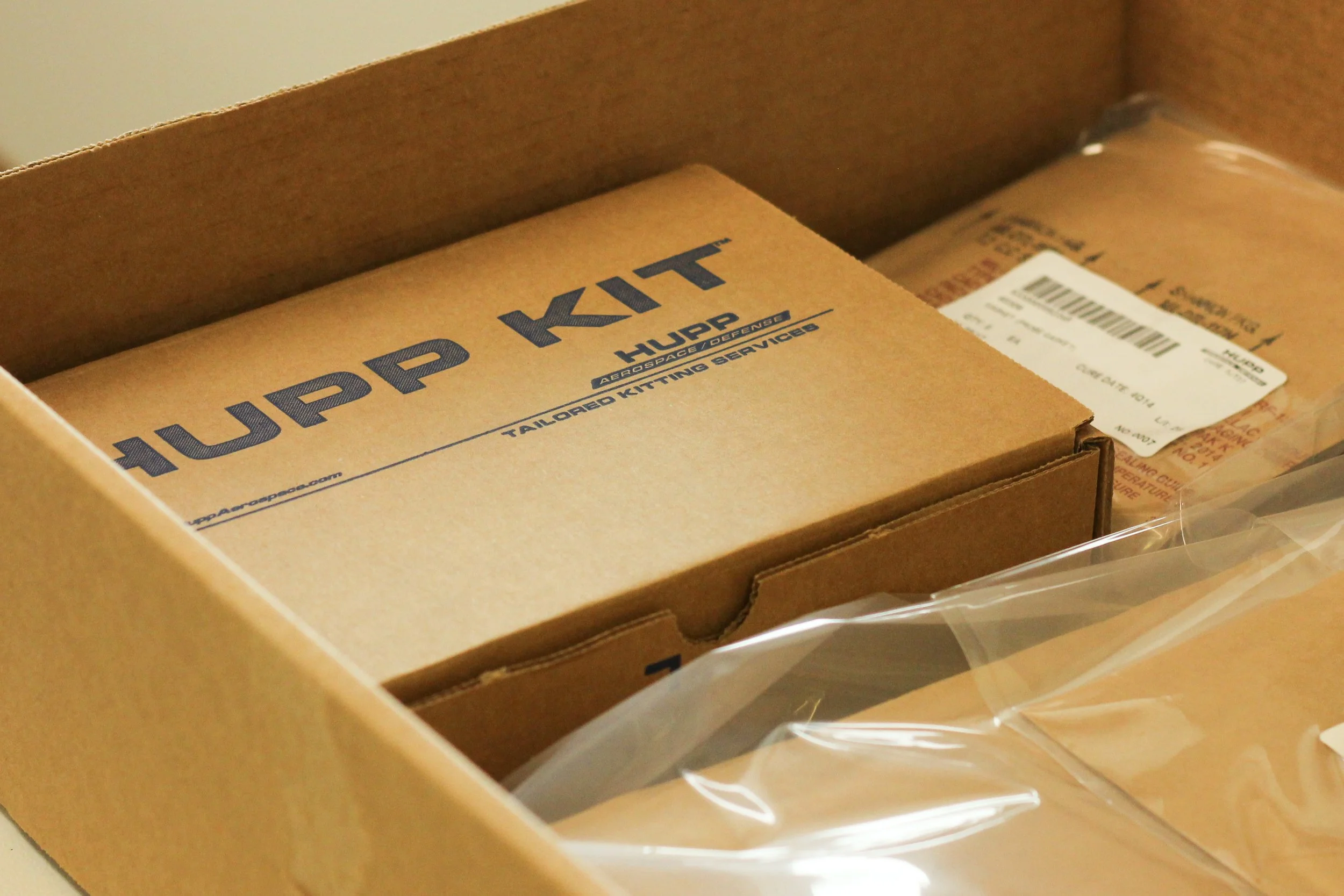 Inside a wire harness prep kit cardboard box containing a brown box with the printed logo 'Upp Kit' and additional text 'HUPP'. There is also a bag with a white label, part of the packaging material is visible.