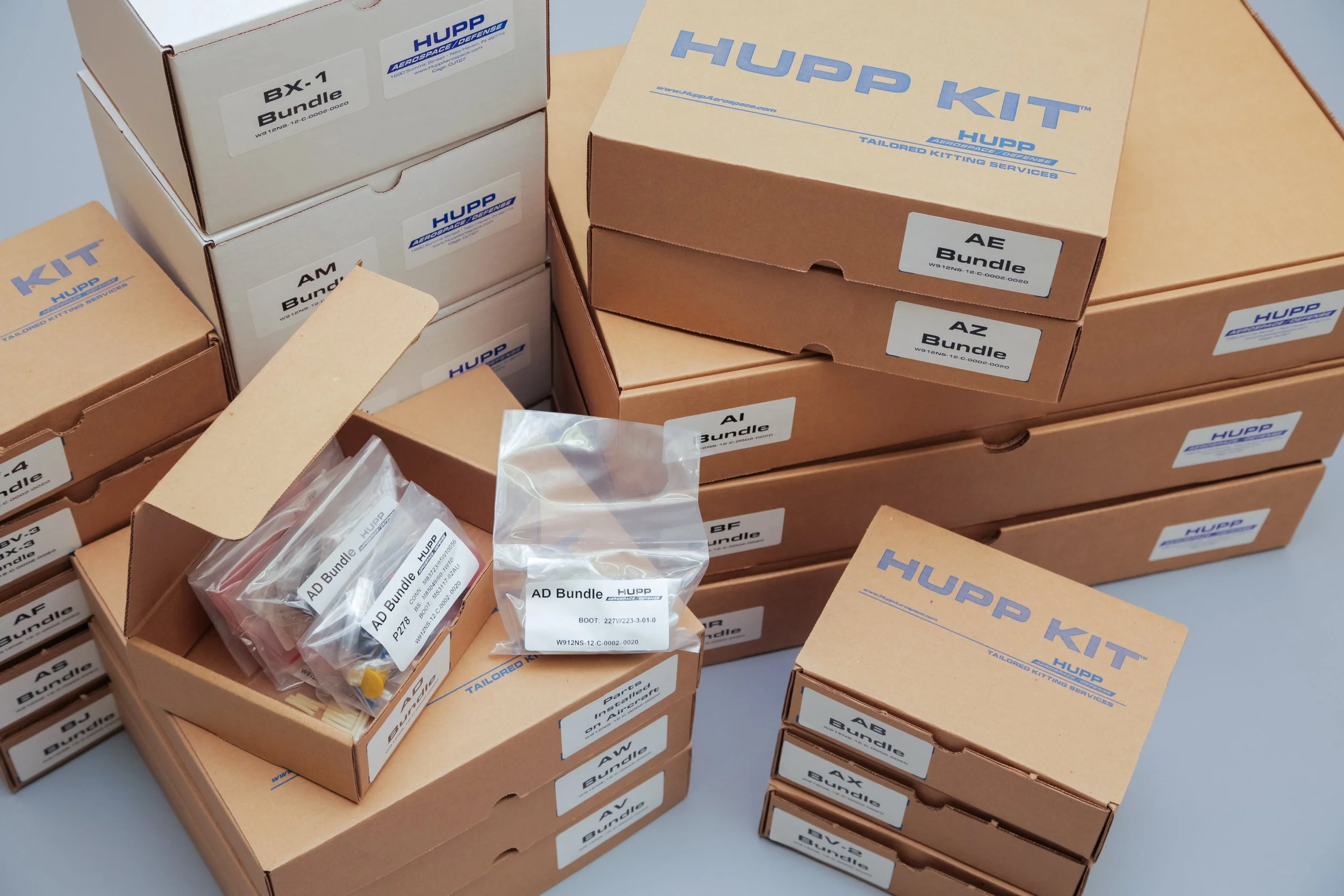 Wire Harness and cable assembly wire prep kits.Multiple cardboard boxes labeled with part numbers and bundle types from Hupp Aerospace Defense, stacked on a flat surface.