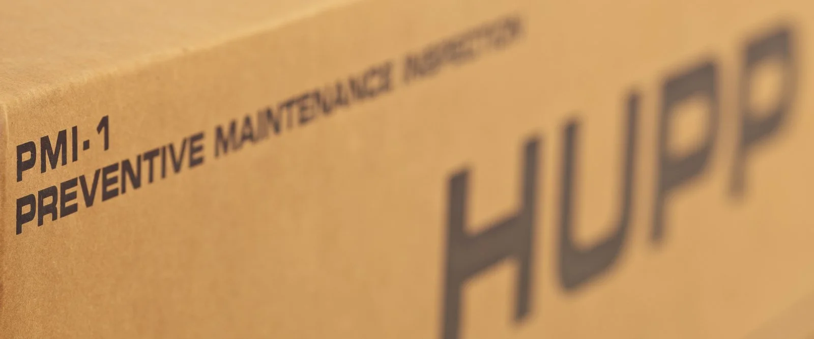 Close-up of a brown cardboard box with black text that says 'PMI-1 PREVENTIVE MAINTENANCE' and the word 'HUPP' visible.