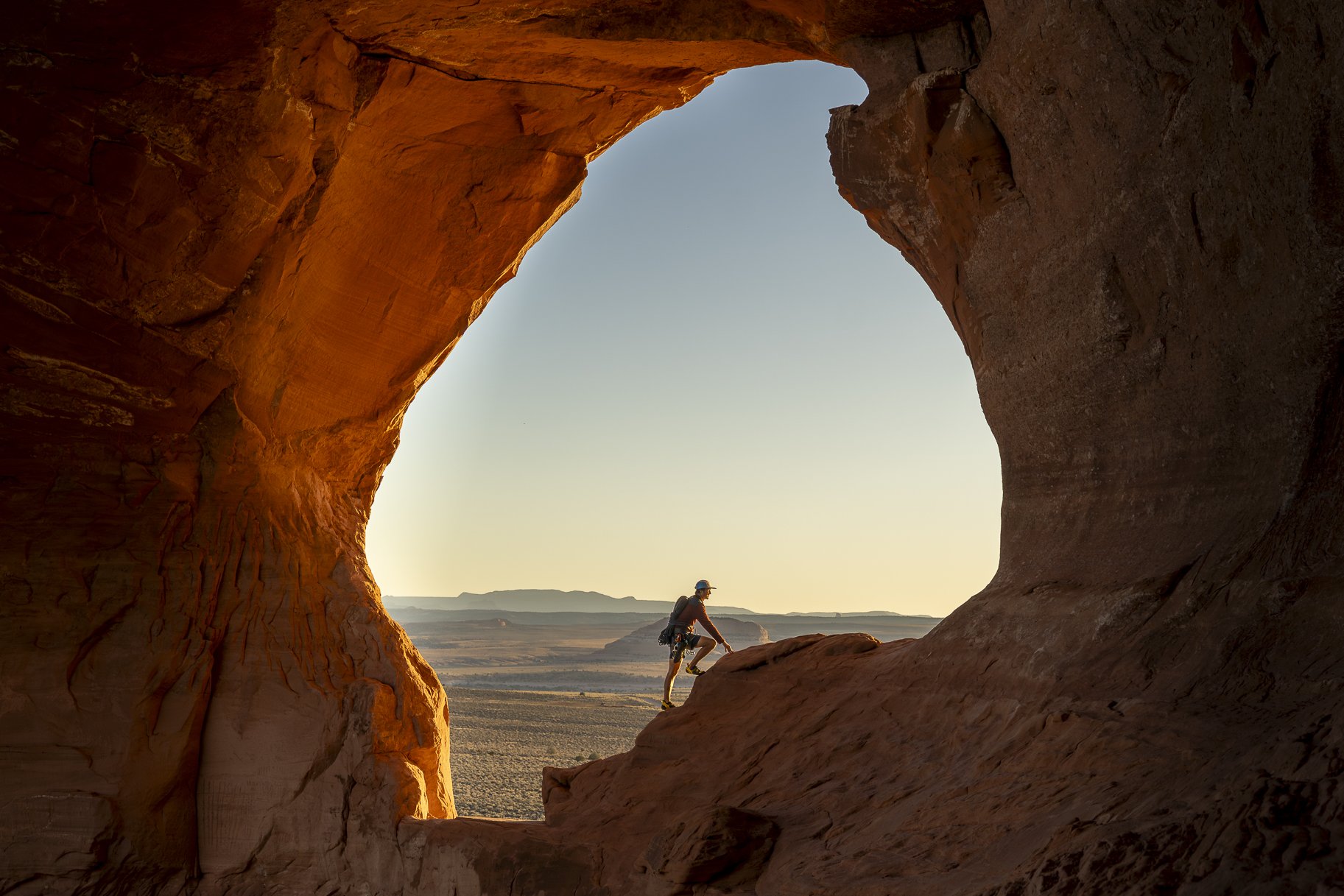 A person climbing on a rock formation at sunset with a scenic desert landscape in the background.