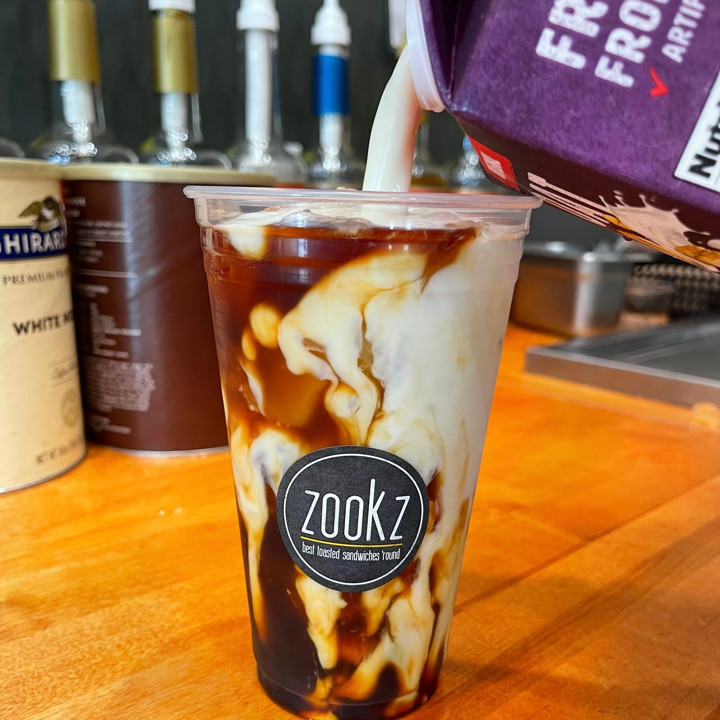 Creamy layered Zookz iced coffee drink in a clear plastic cup with the Zookz logo..JPEG