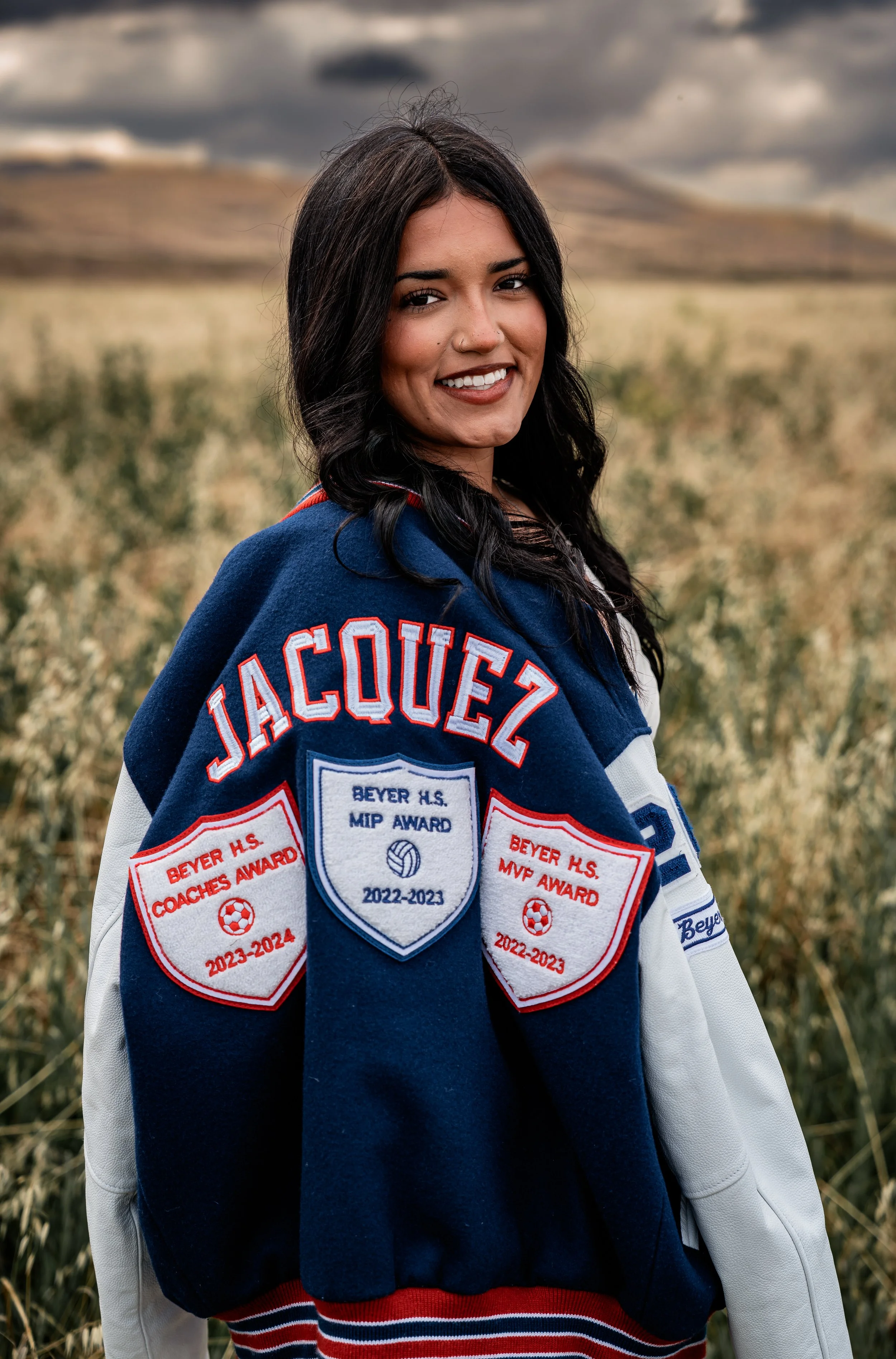 High school senior posing with her letterman in an open field. Photo taken in Patterson, CA by Mikaela Tosta Photography