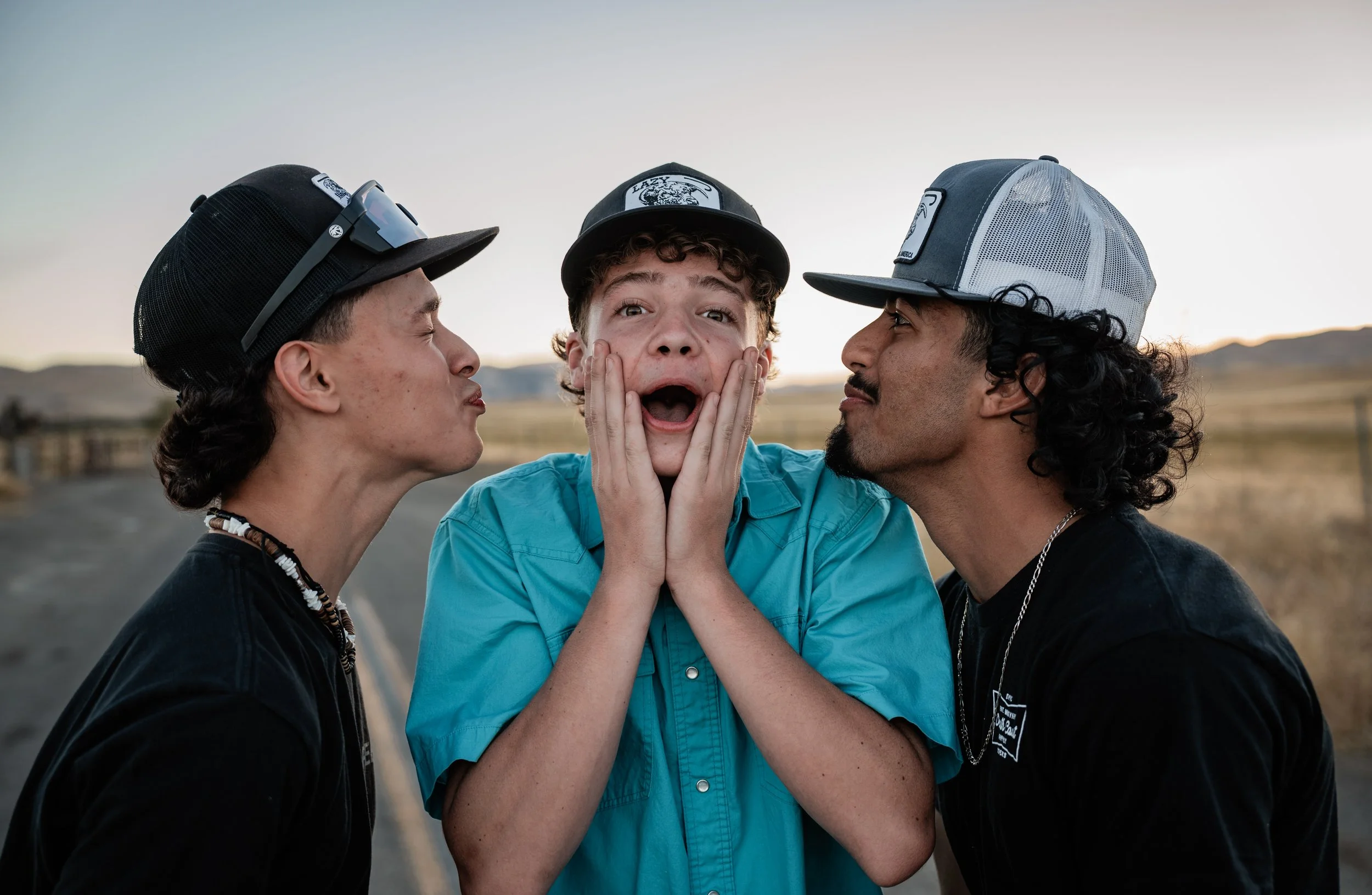 Three boys doing a funny photo. Middle boy has a shocked expression while the other two try to kiss his cheeks. Photo taken in Newman, CA by Mikaela Tosta Photography.