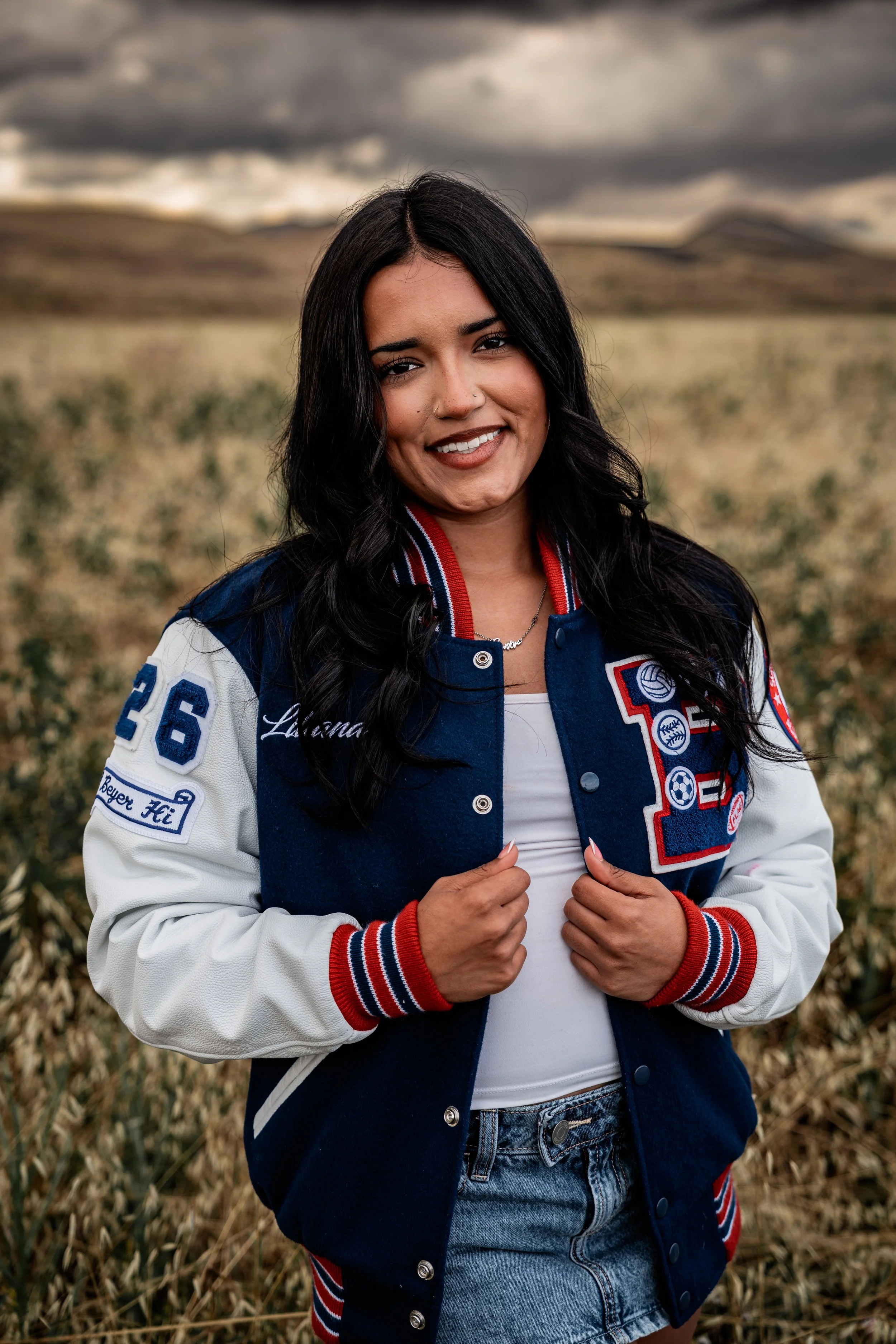 High school senior posing with her letterman in an open field. Photo taken in Patterson, CA by Mikaela Tosta Photography