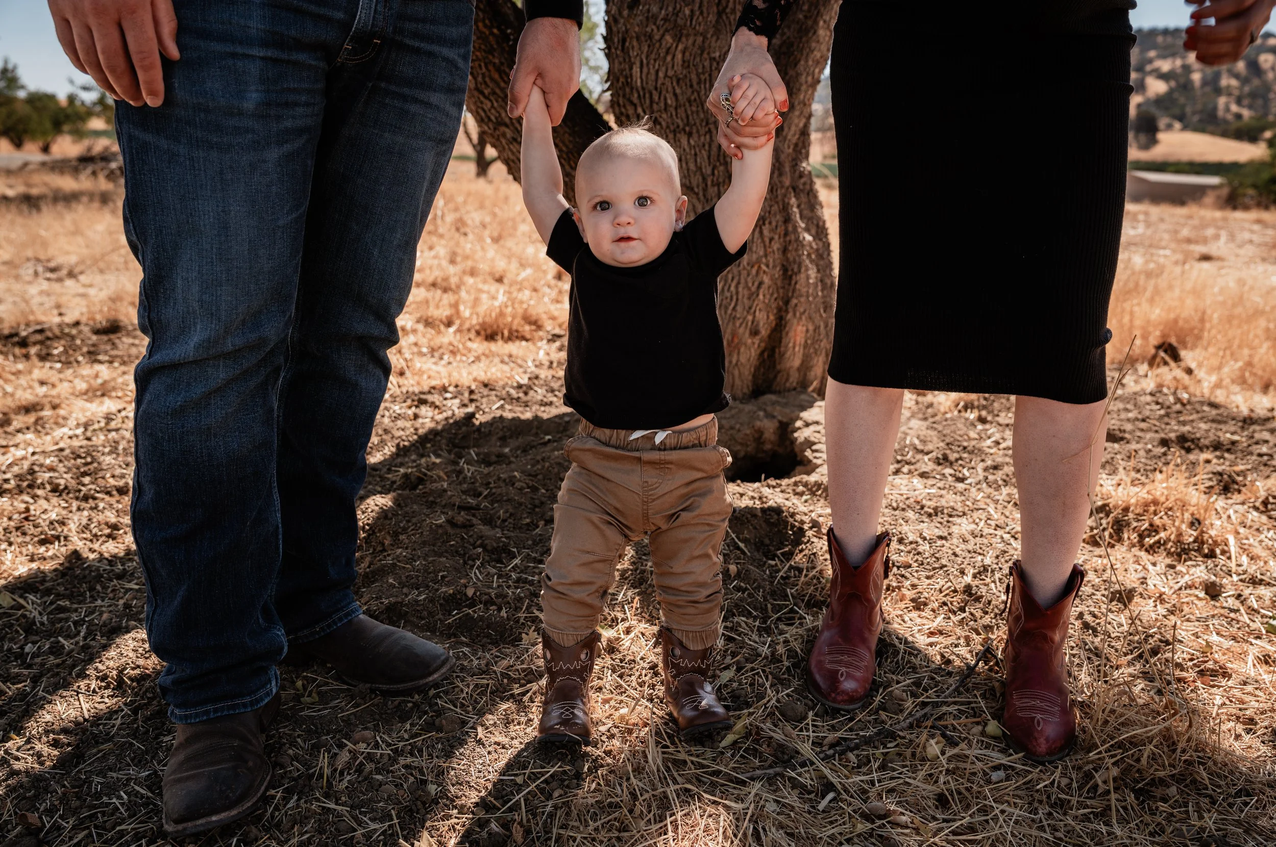 Parents holding sons hands, with the frame focusing in the son and the parents legs in Capay, CA. Photo taken by maternity photographer, Mikaela Tosta Photography.